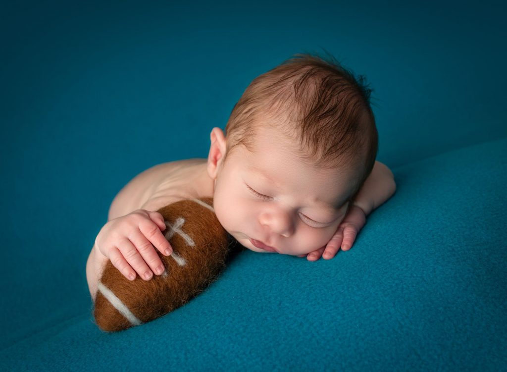 newborn baby boy sleeping with a football tucked underneath his hand