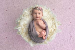 3 month old baby girl swaddled in a white bowl of fluff on pink background wide awake