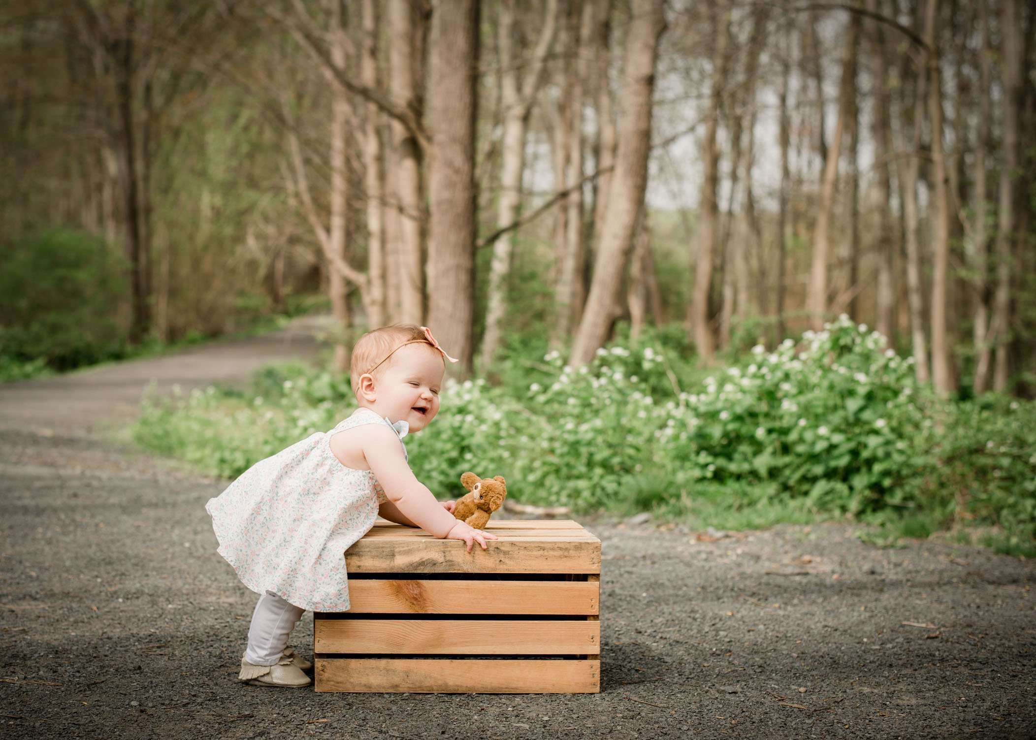 9 mo old baby girl leaning on wooden crate on path