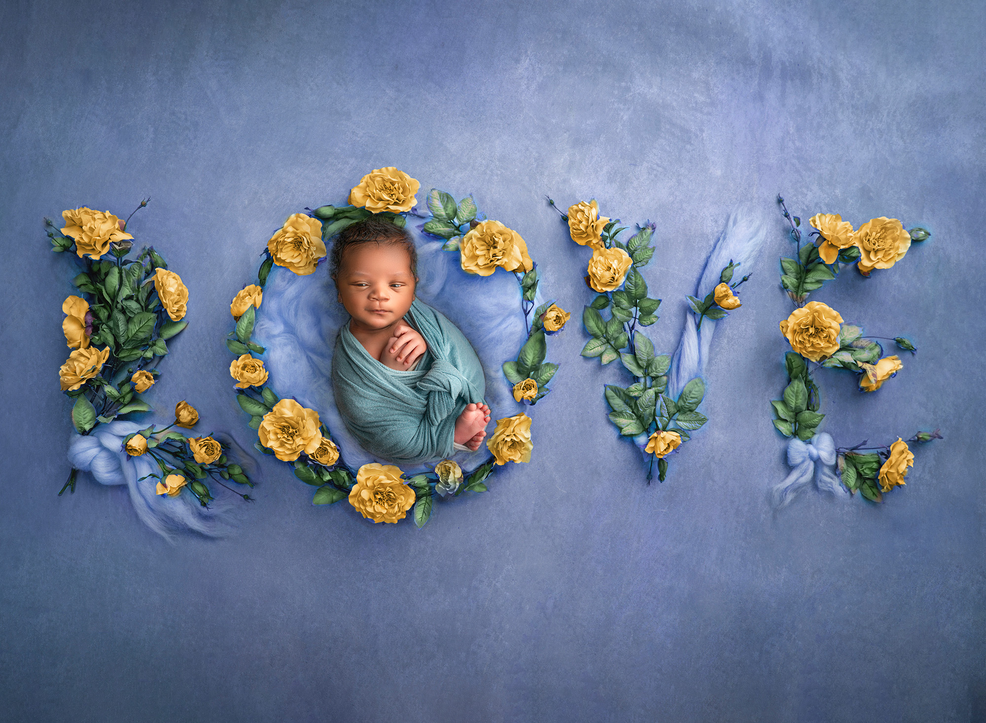 newborn lying in the center of the word "love" made of roses and blue fluff.