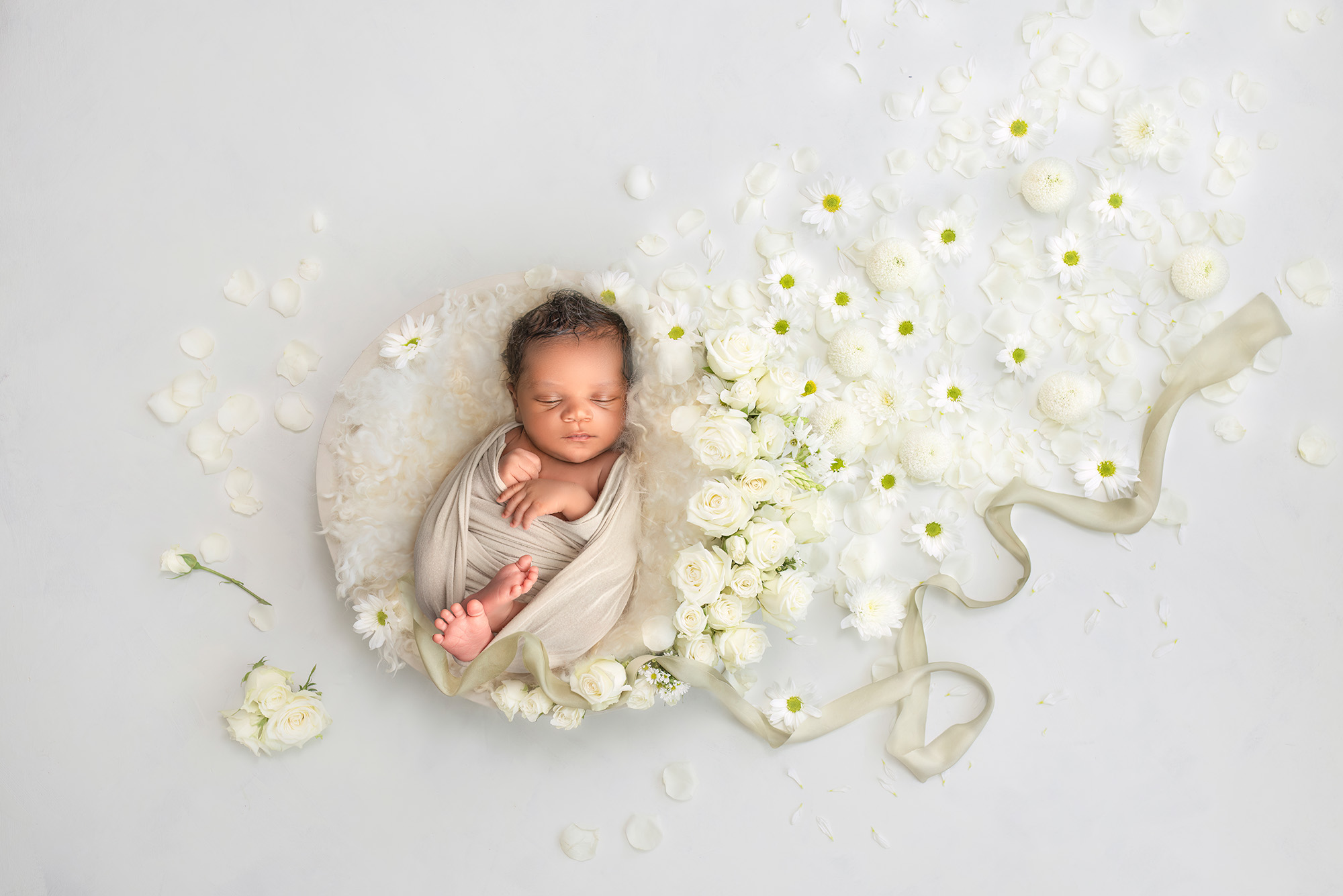 newborn photo studio newborn sleeping peacefully in a bowl surrounded by white roses, daisies, and a tan ribbon