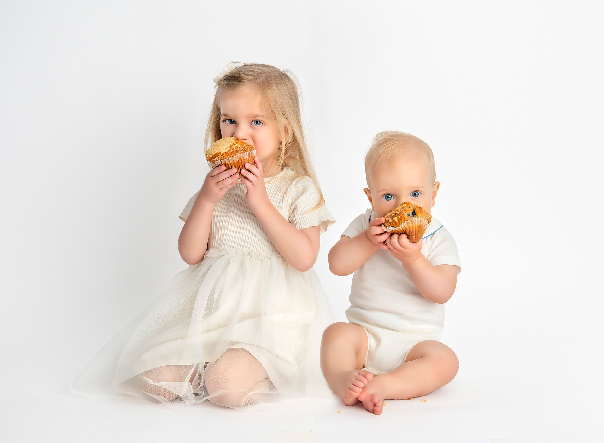 All White Baby Milestone Smash Photoshoot baby and sister eating a blueberry muffin on a white background