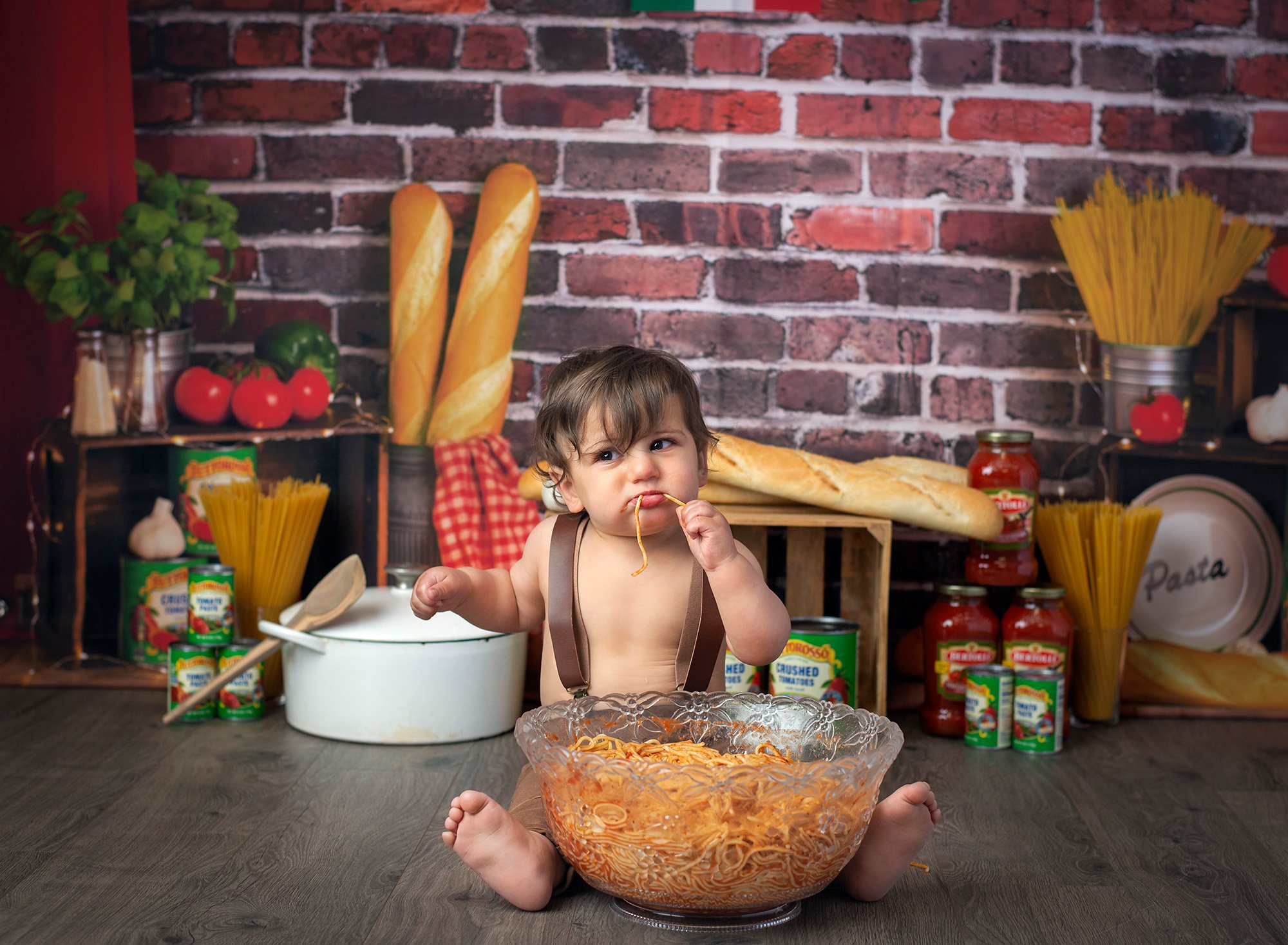 one year old boy eating spaghetti with Italian bread and jars of sauce in background
