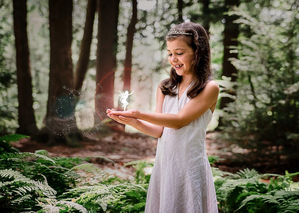 little brown haired girl holding a light fairy in her hands in the woods