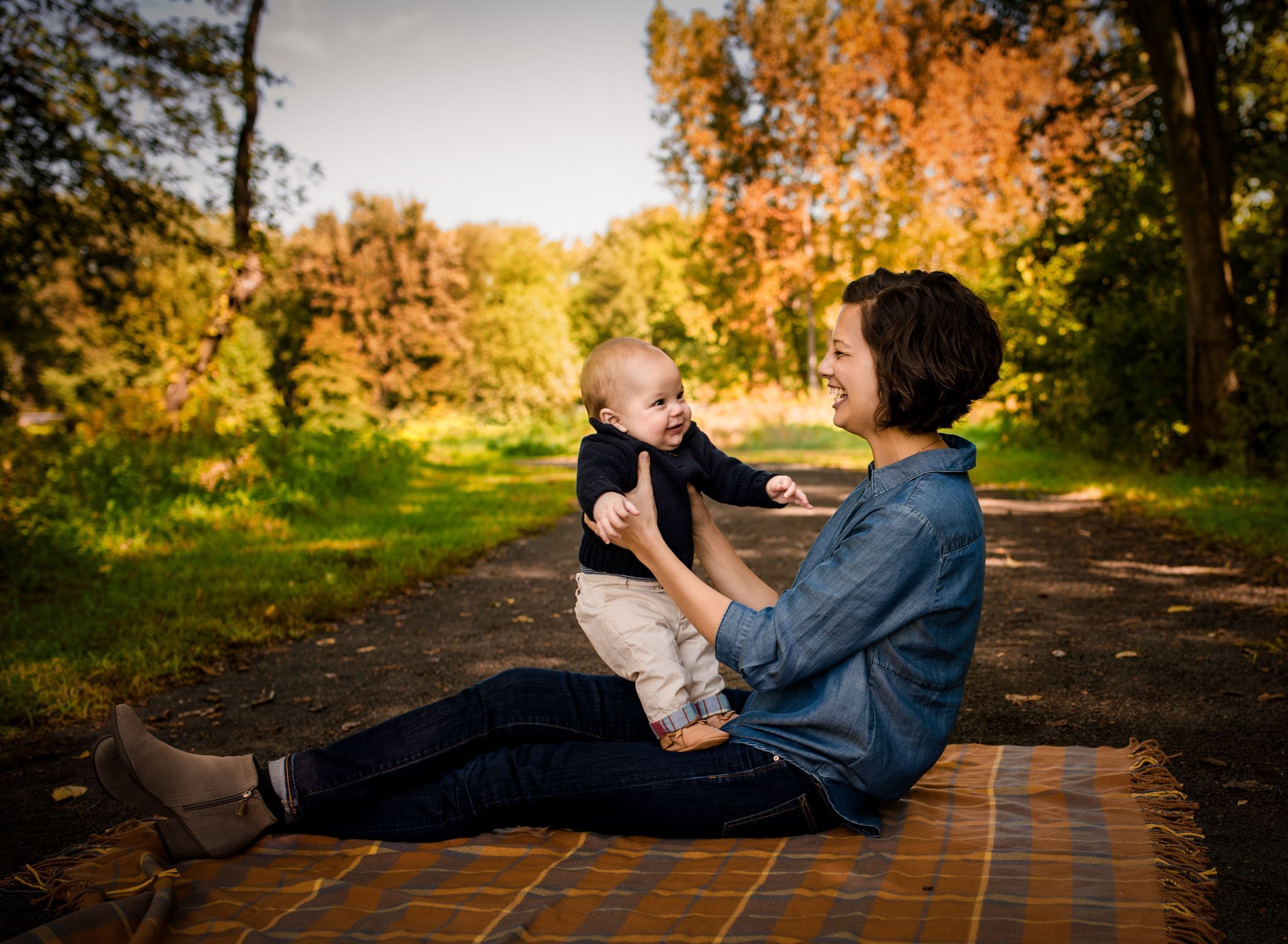 Mom playing with 6 month old baby boy on her lap on a path outside in fall