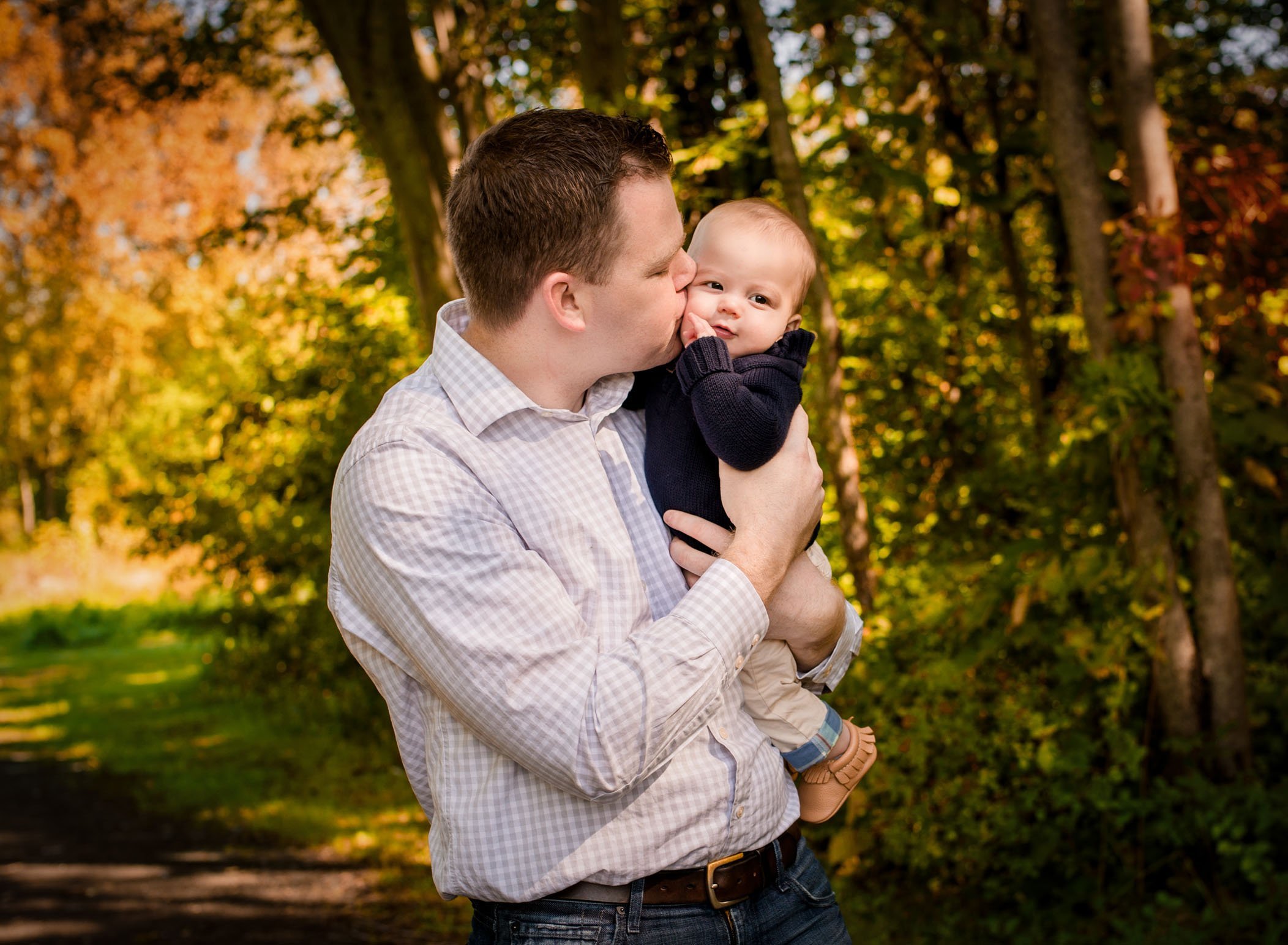 Dad kissing 6 month old son's cheek while holding him outside in fall