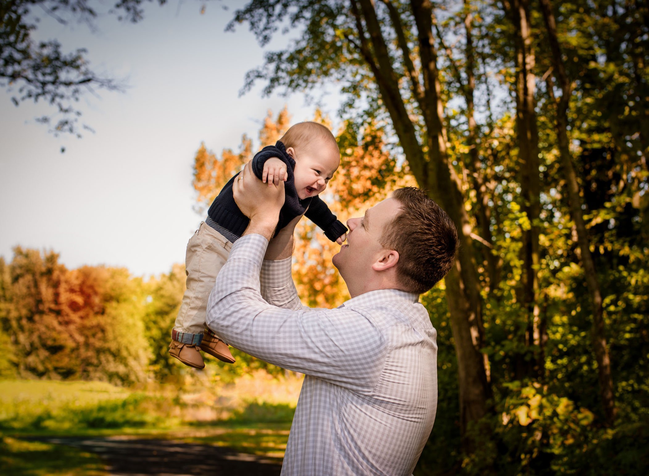 Dad holding 6 month old baby boy in air and baby laughing outside in fall