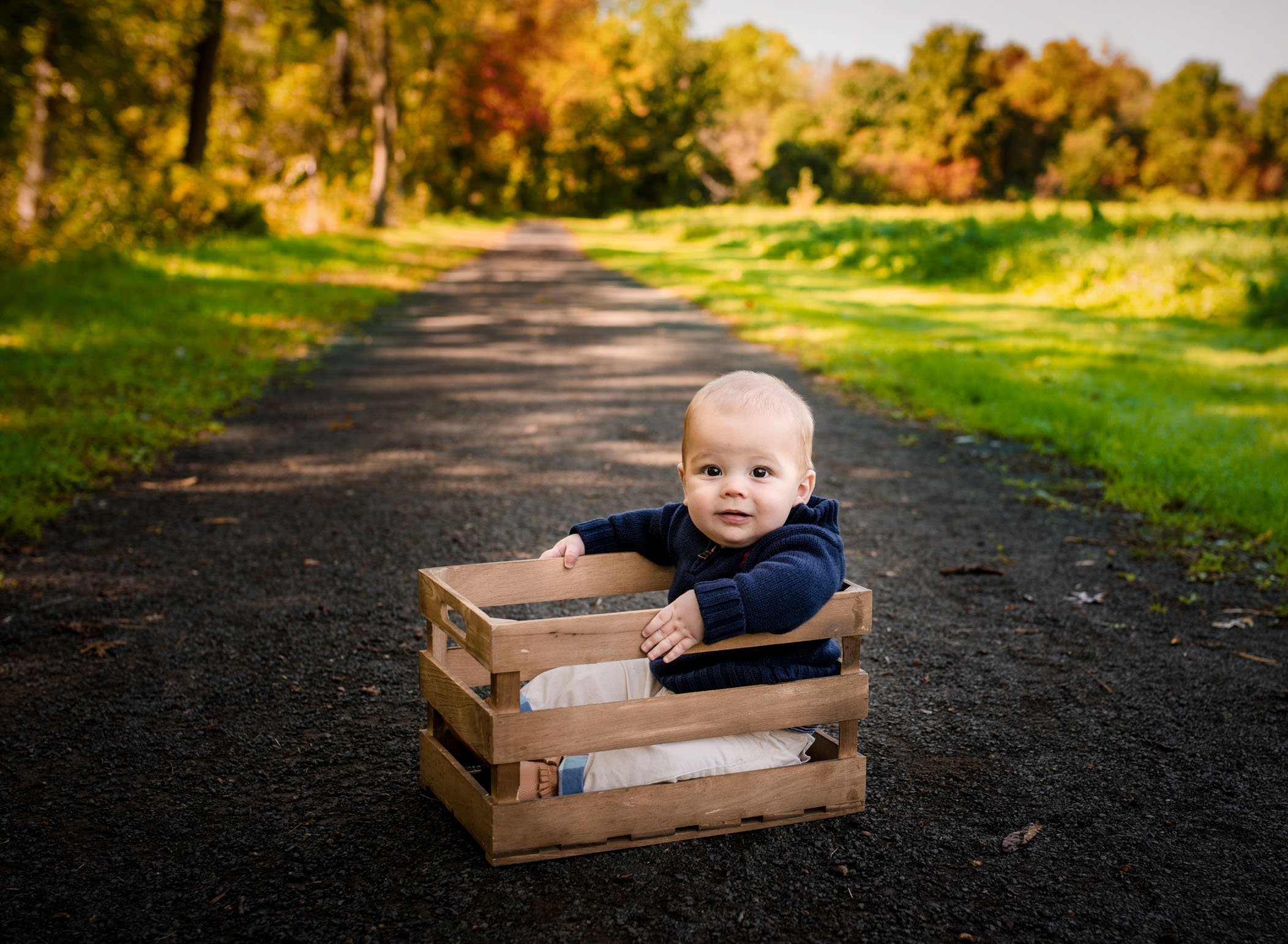 6 month old boy sitting in a crate outside on a path in fall