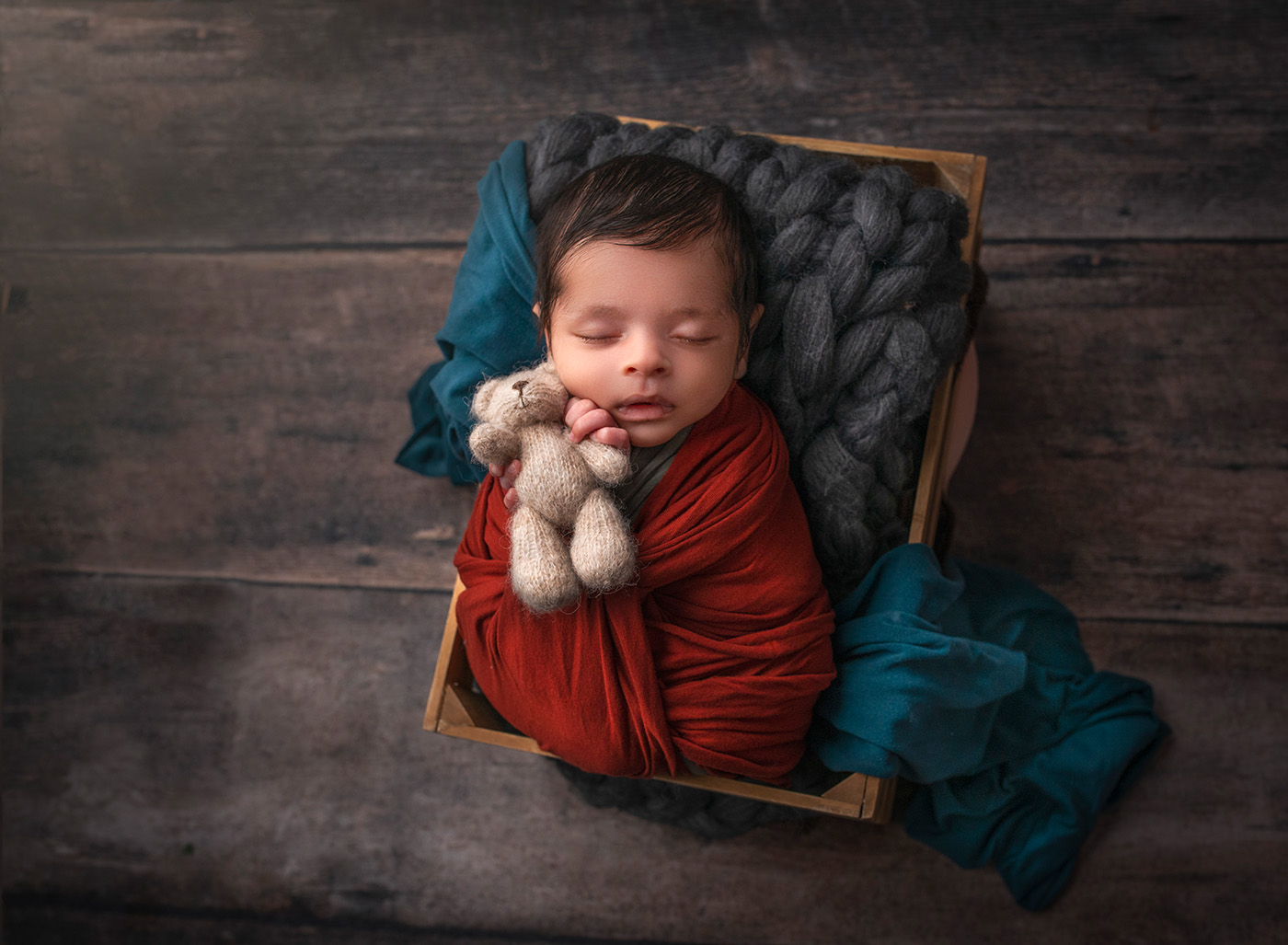 newborn baby sleeping in a crate holding a teddy bear