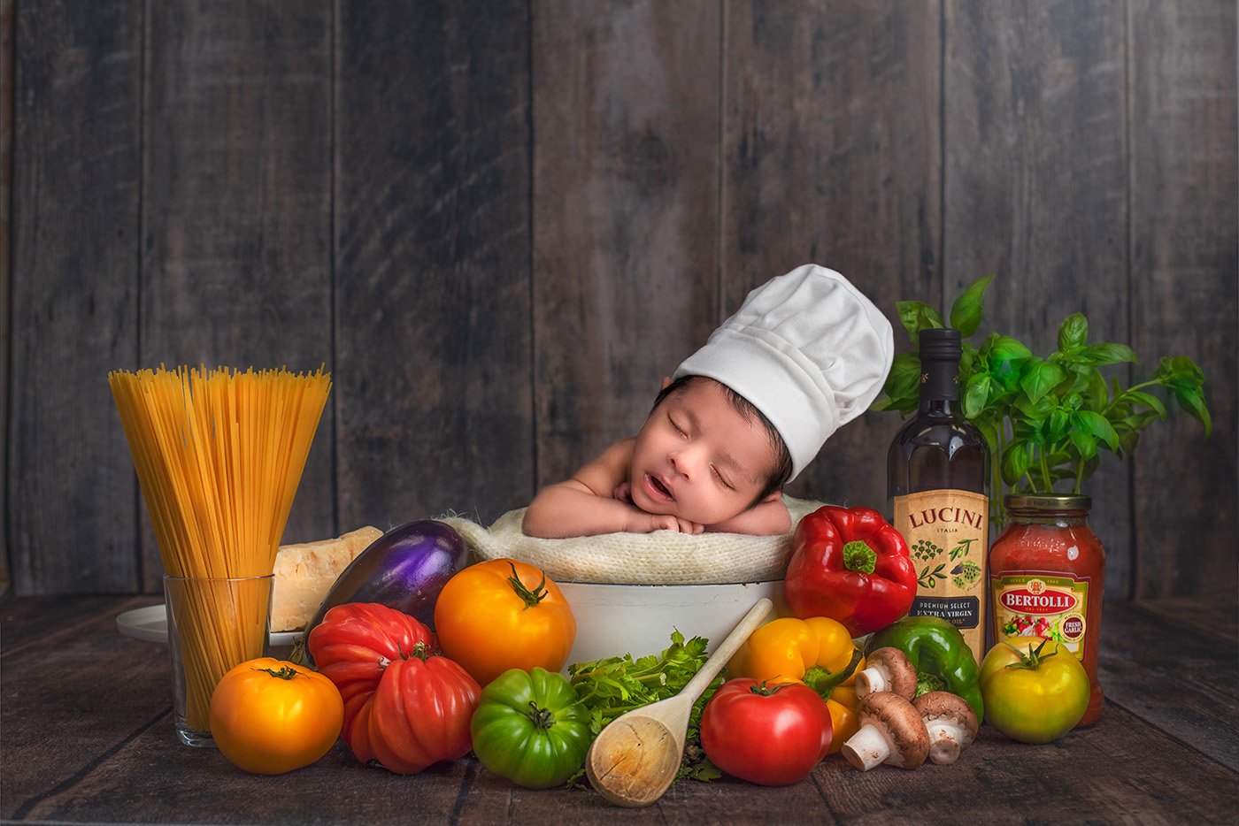 Newborn sleeping in pot with Italian dinner ingredients.