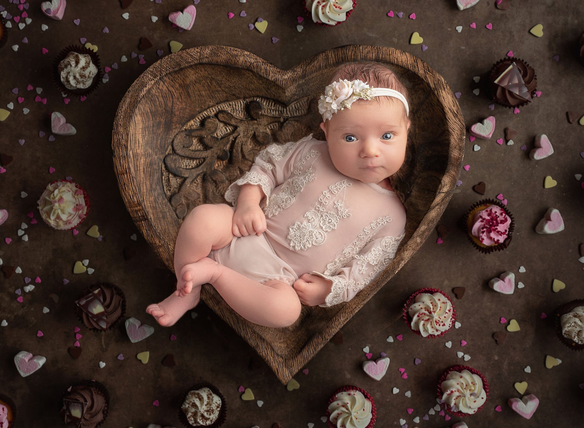best time to take newborn photos 5 week old baby girl lying in a heart shaped bowl surrounded by cupcakes looking at the camera best time to take newborn photos