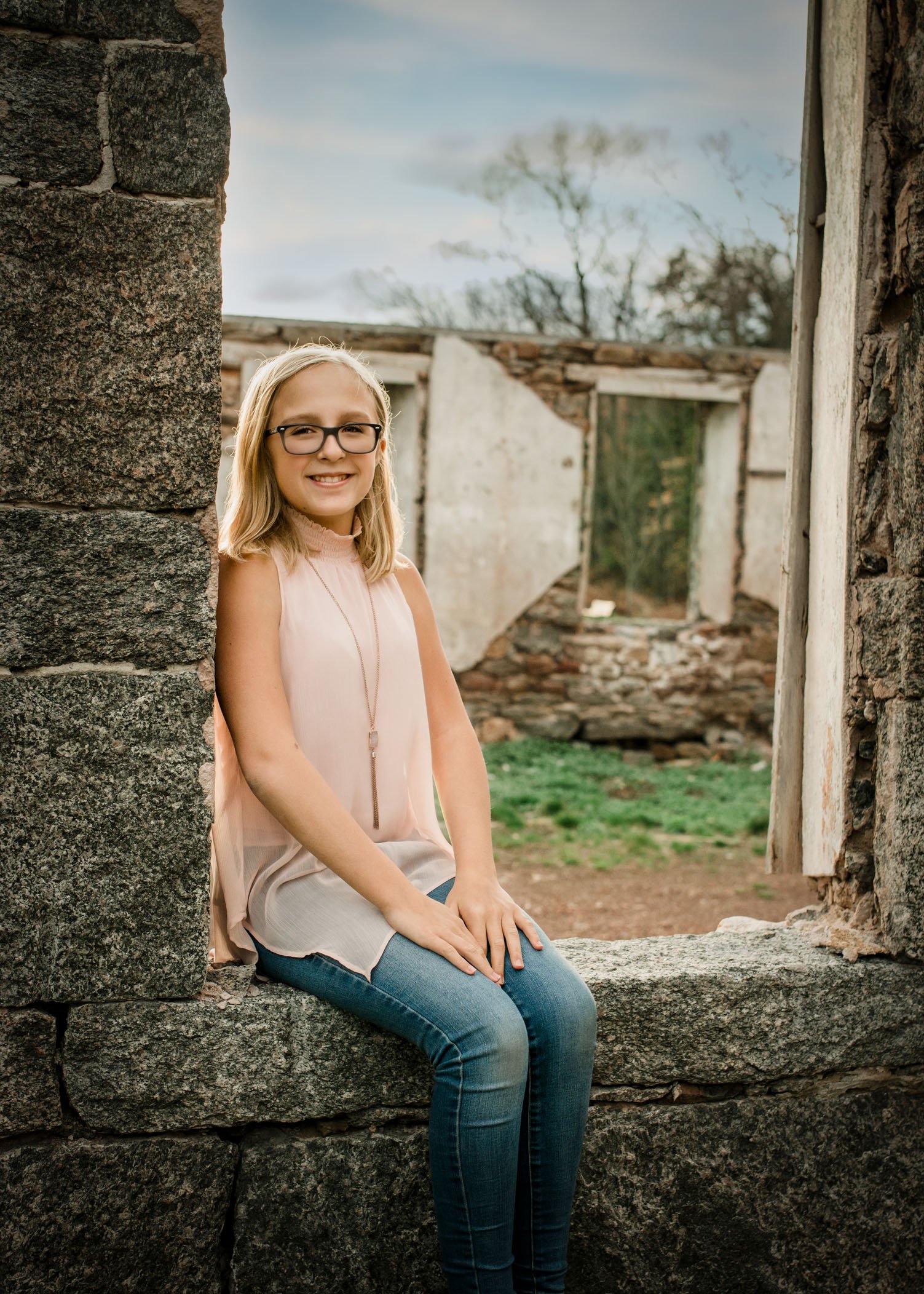 Tween girl sits smiling in old window opening of building ruins