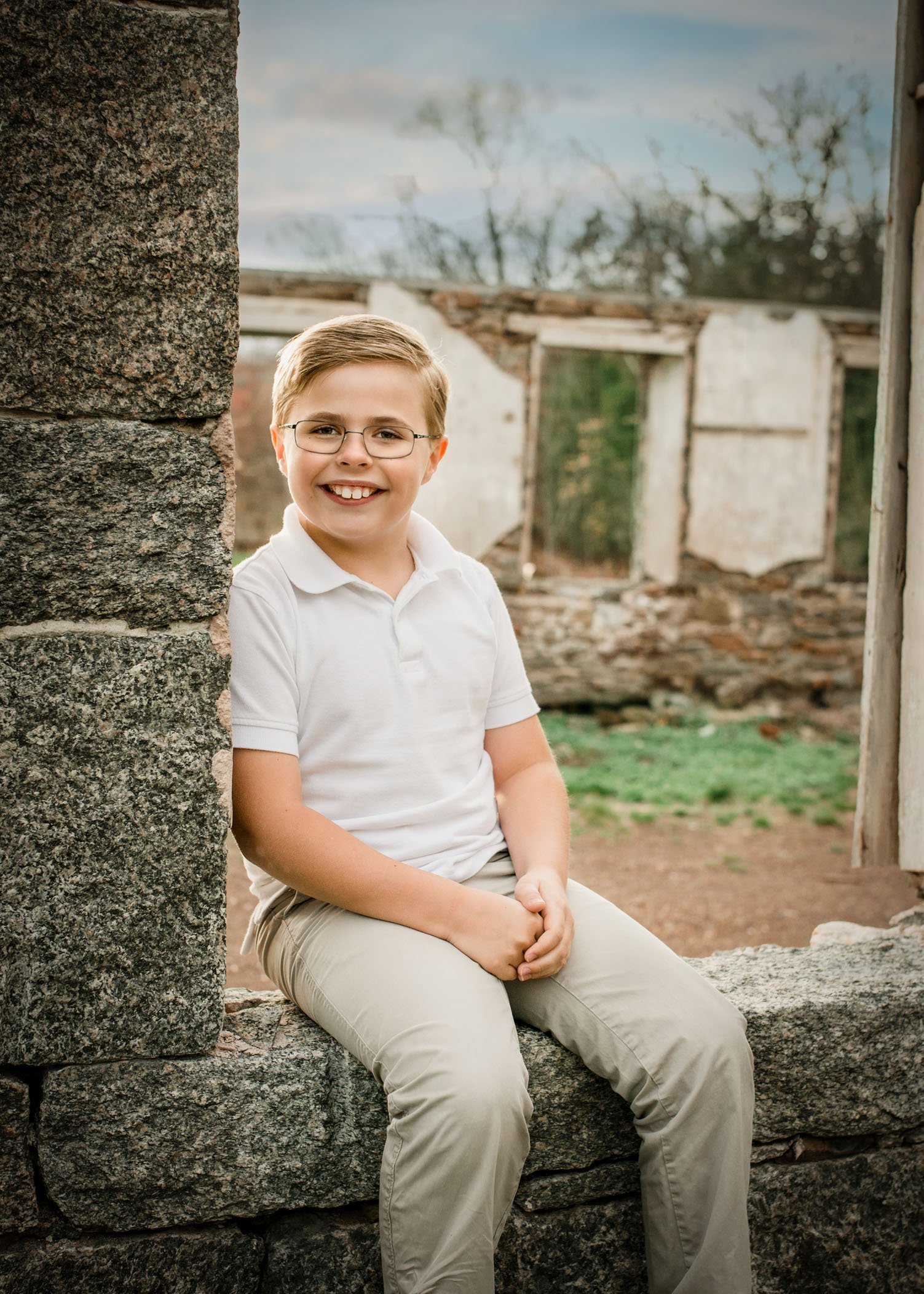 8 year old boy sits smiling in old window opening of building ruins smiling