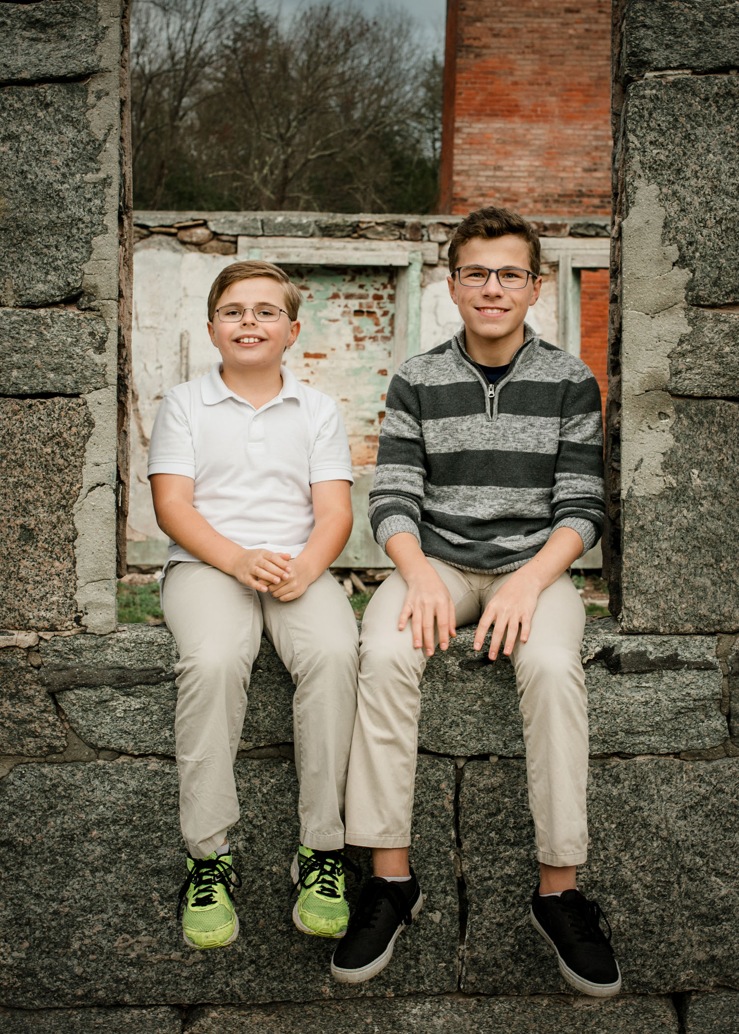 Two young brothers sit on a wall at building ruins