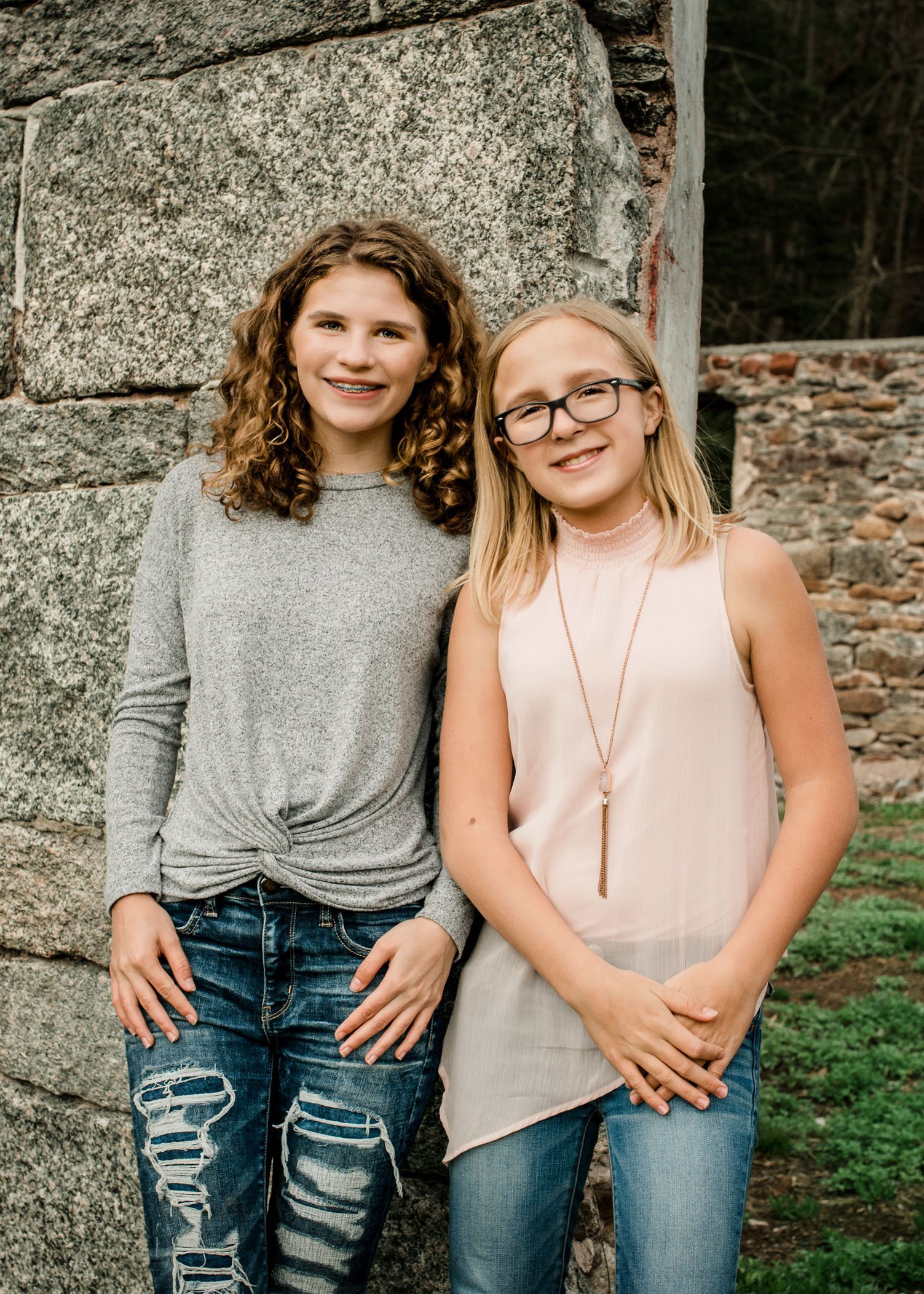 Two tween sisters stand smiling next to building ruins