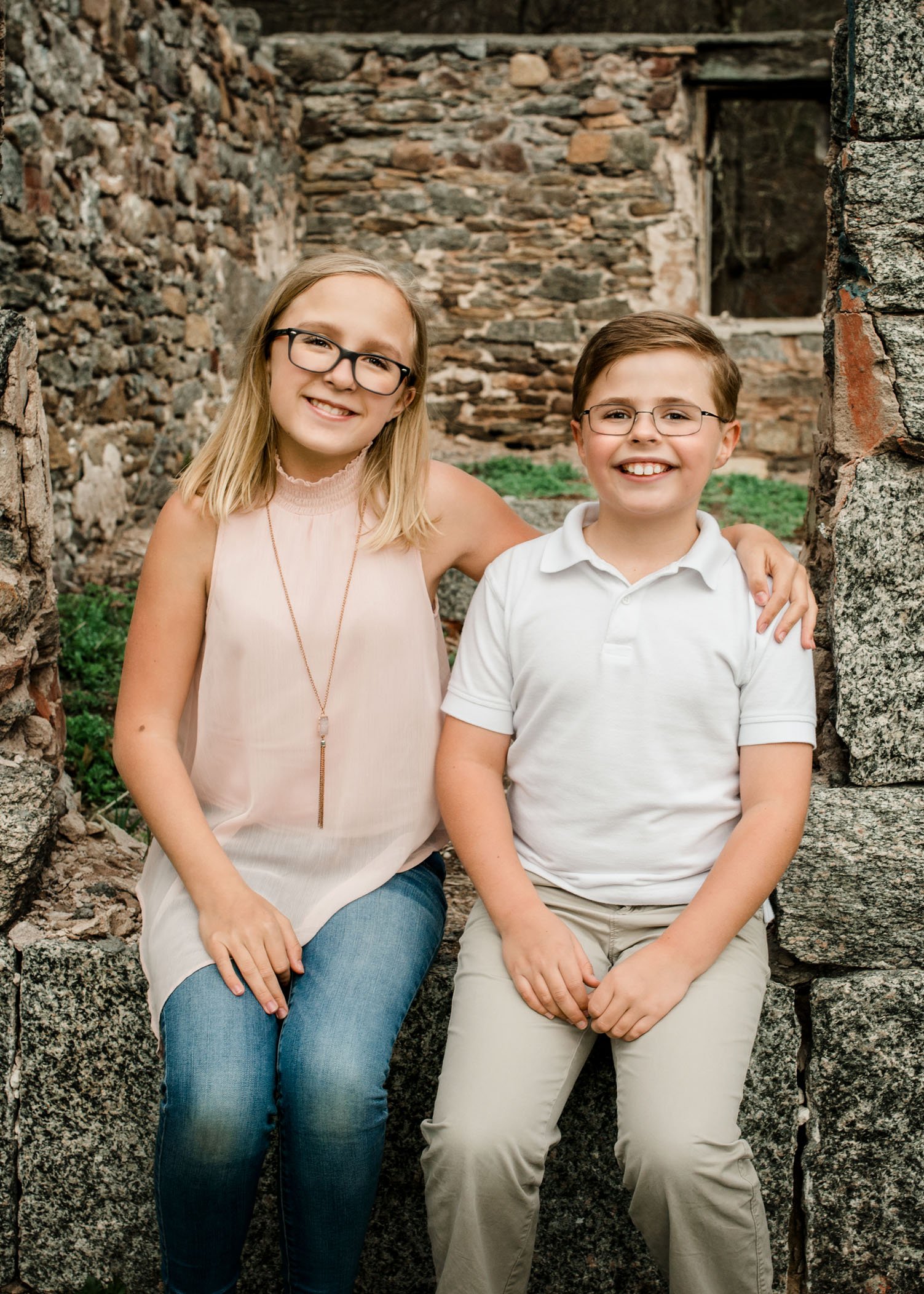 Sister and brother sit on building ruins smiling together