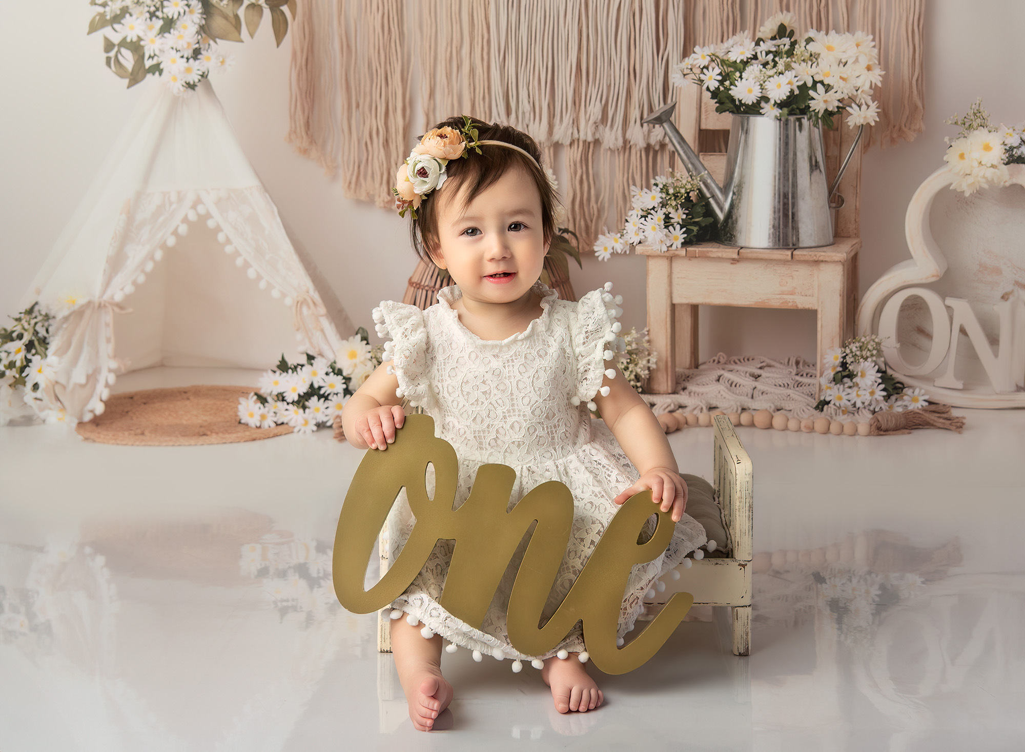 Boho 1 Year Old Photos Sophie sitting on a small, painted bed, holding a gold "ONE" sign