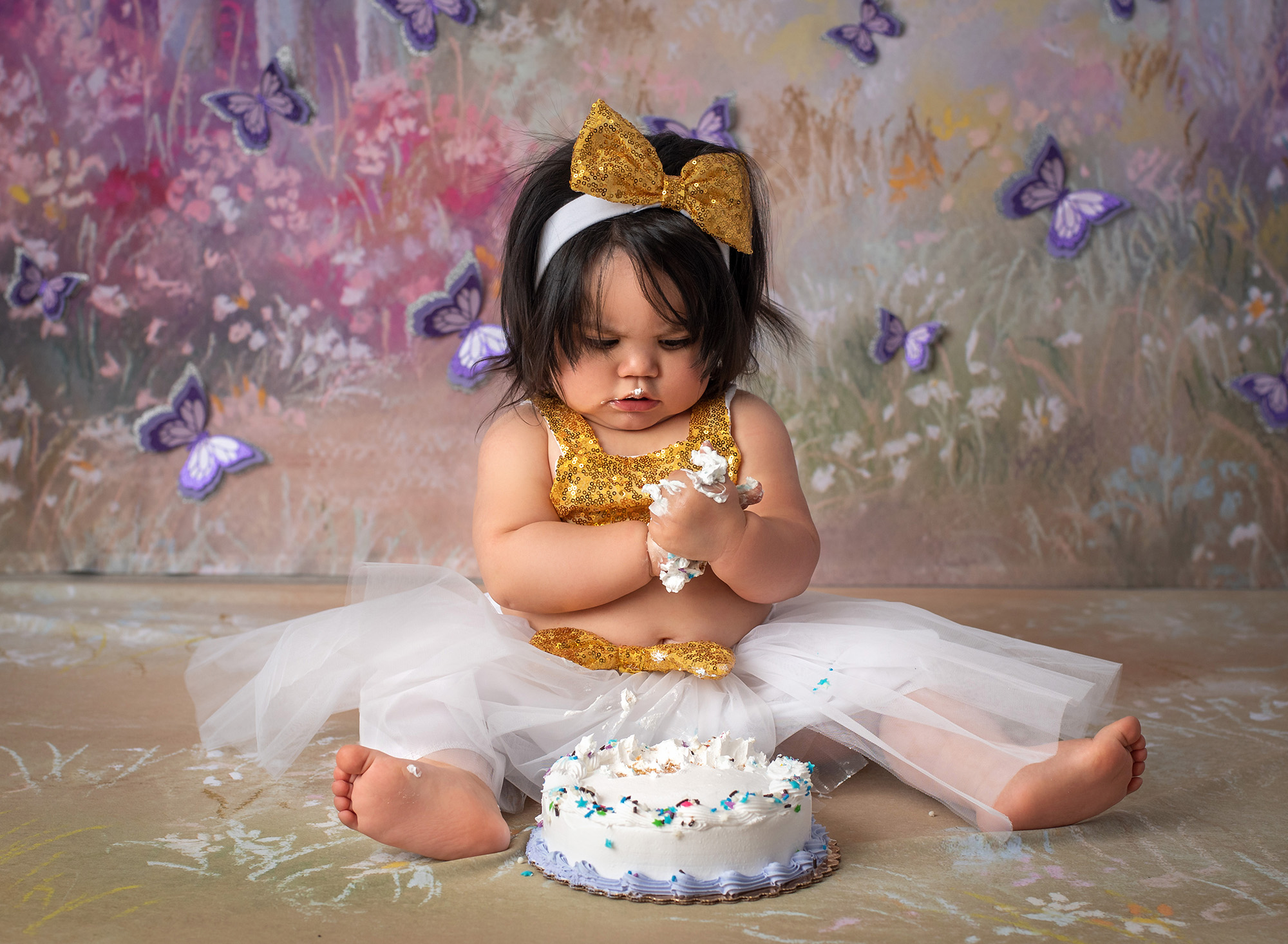 Butterfly Cake Smash Pictures one year old girl rubbing cake in hands with butterfly background