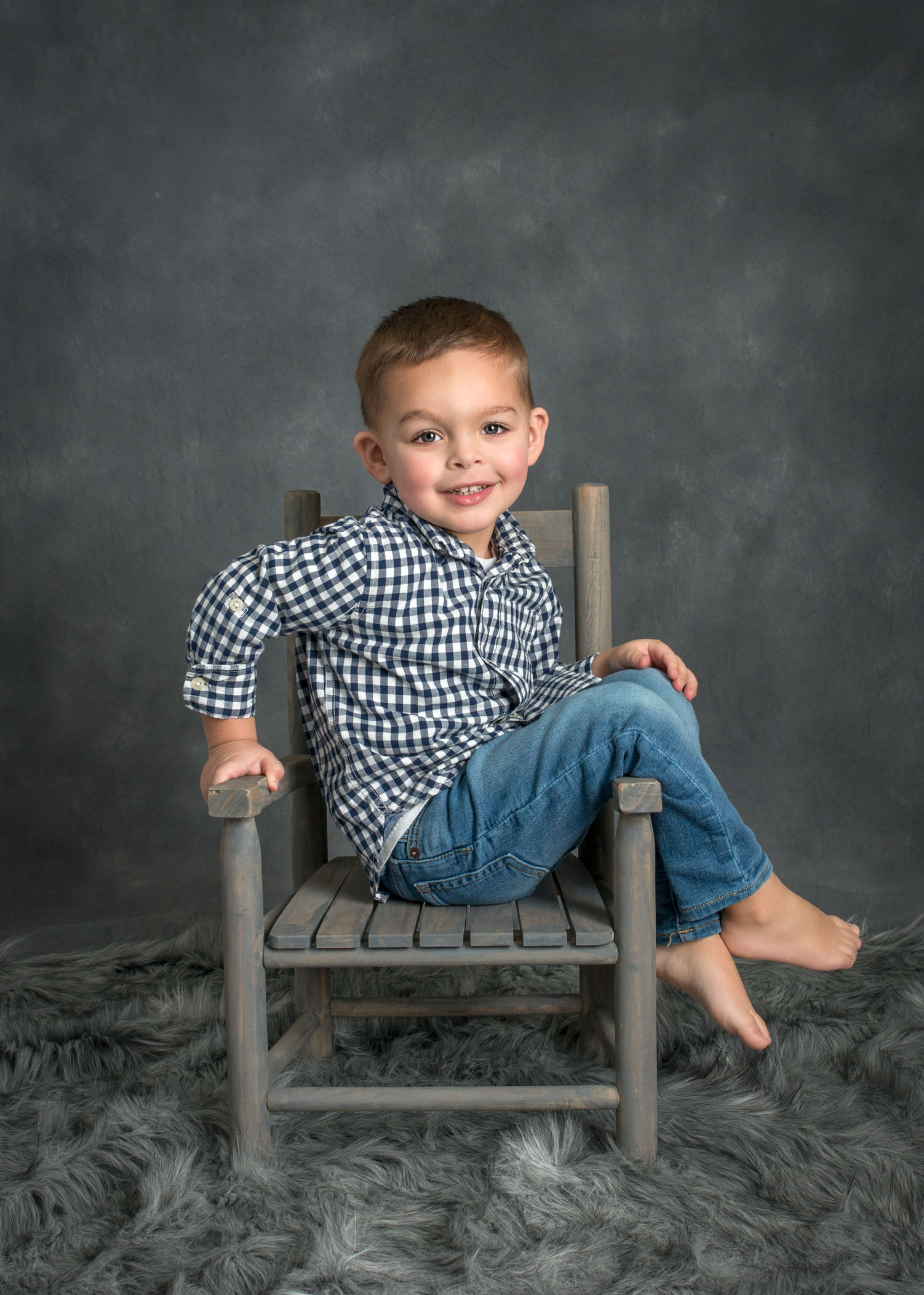 3 year old boy sitting in small wooden chair sideways smiling