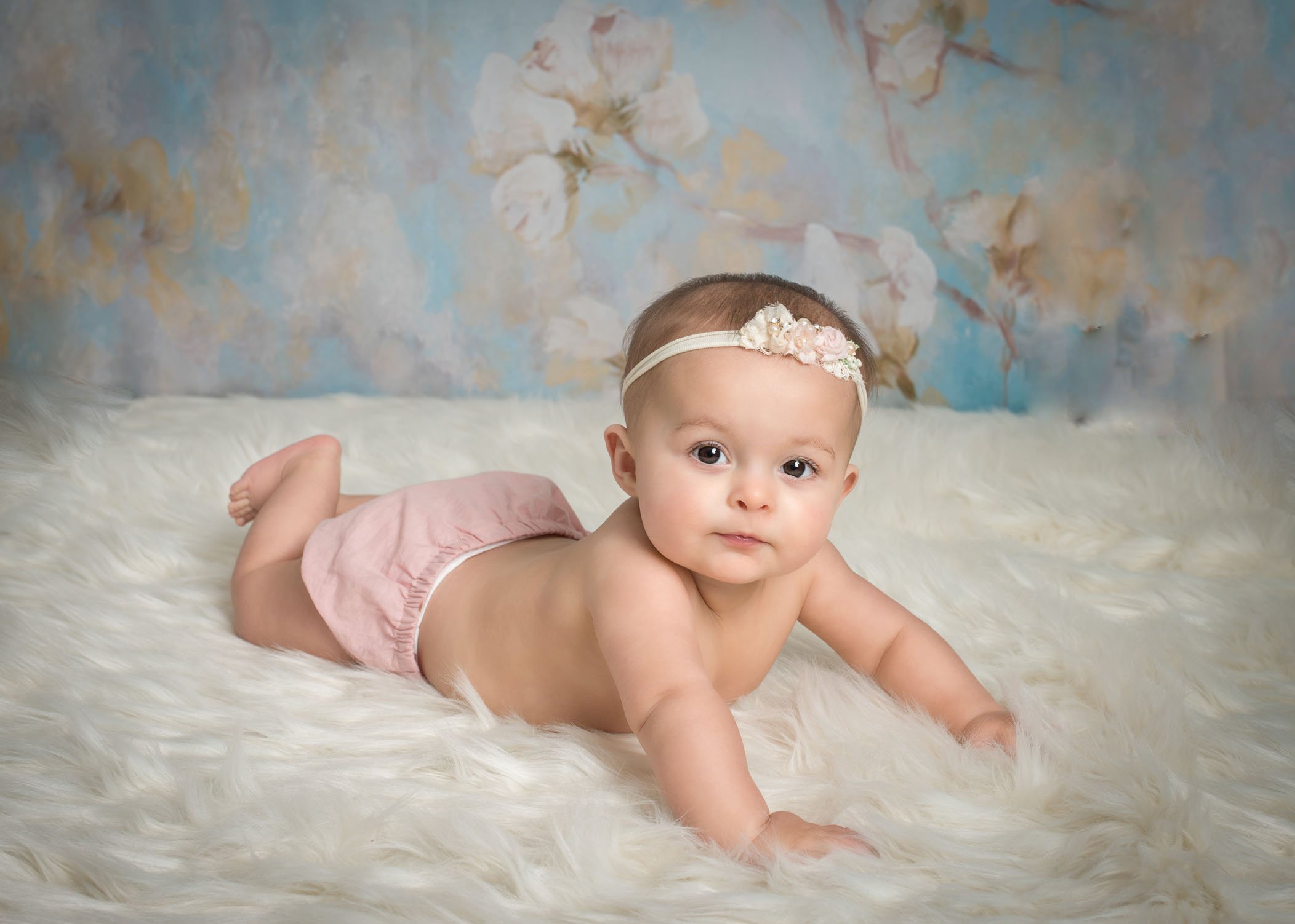 6 month old baby girl lying on white fur with headband on looking at the camera