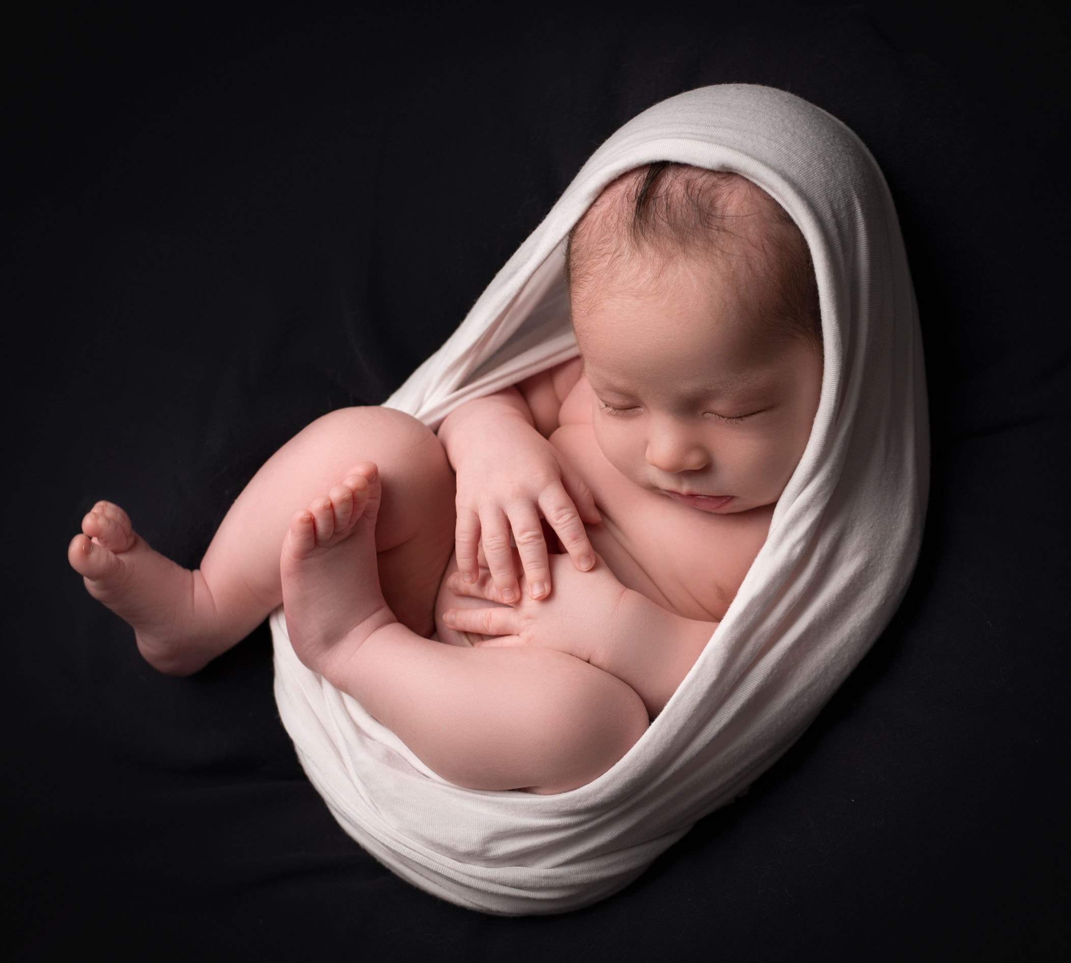 newborn baby boy in egg wrap on black background