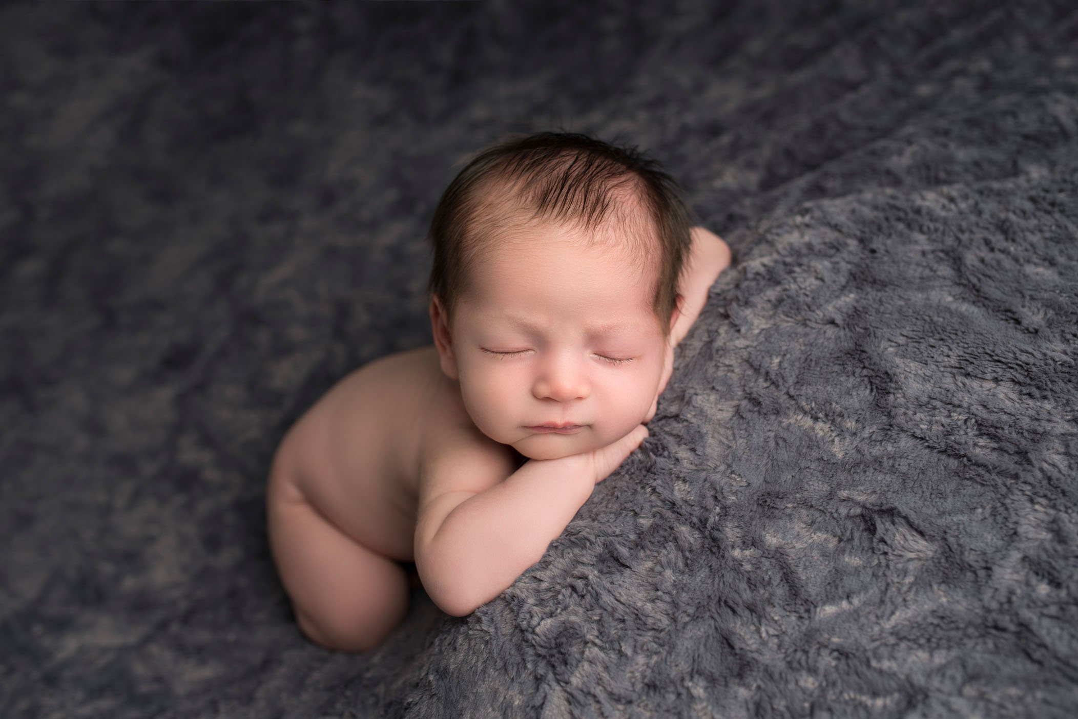 newborn baby boy sleeping on grey with head on hands