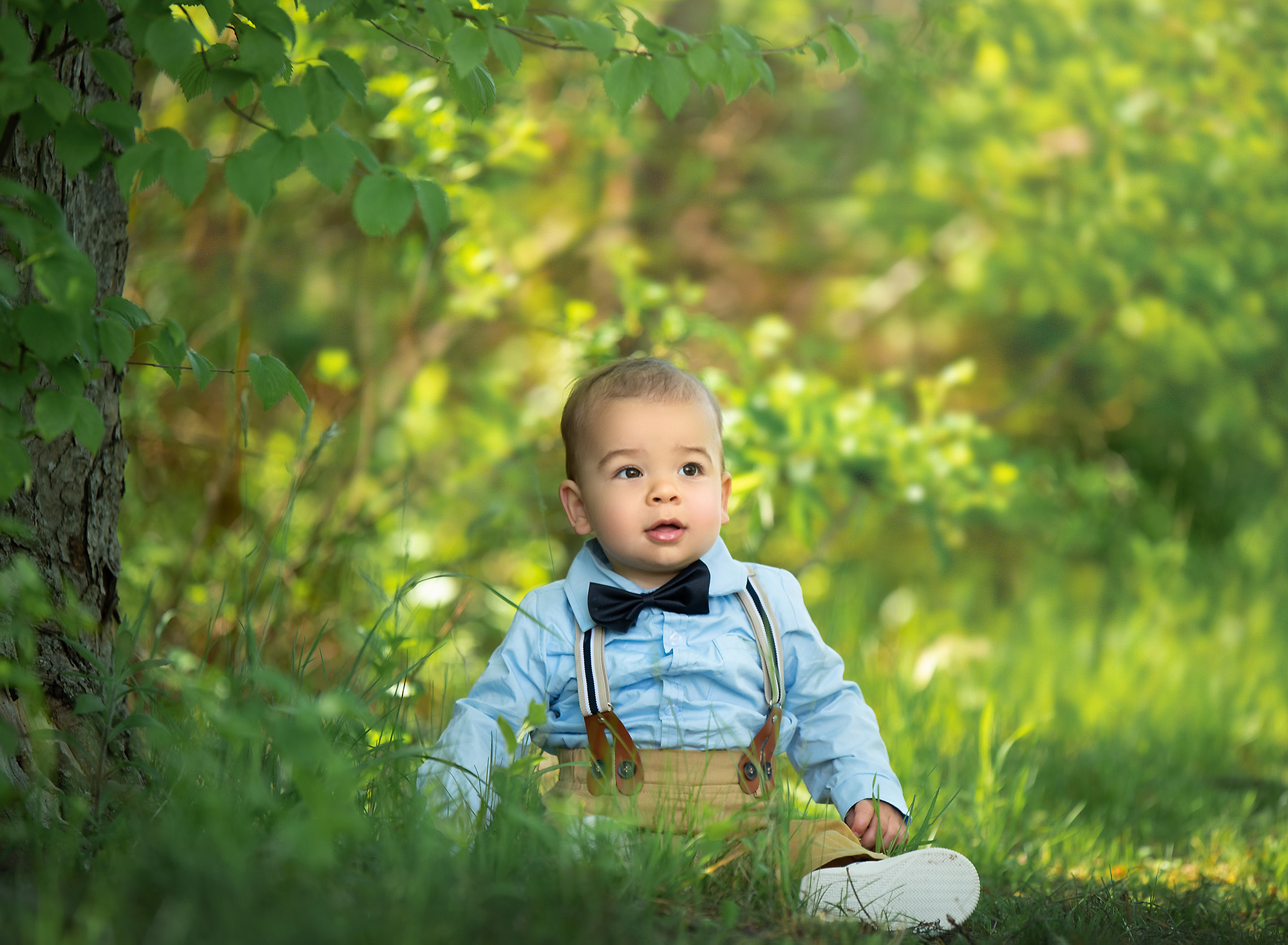 Summer Family Photosinfant boy sitting on the grass smiling wearing a bow tie and suspenders