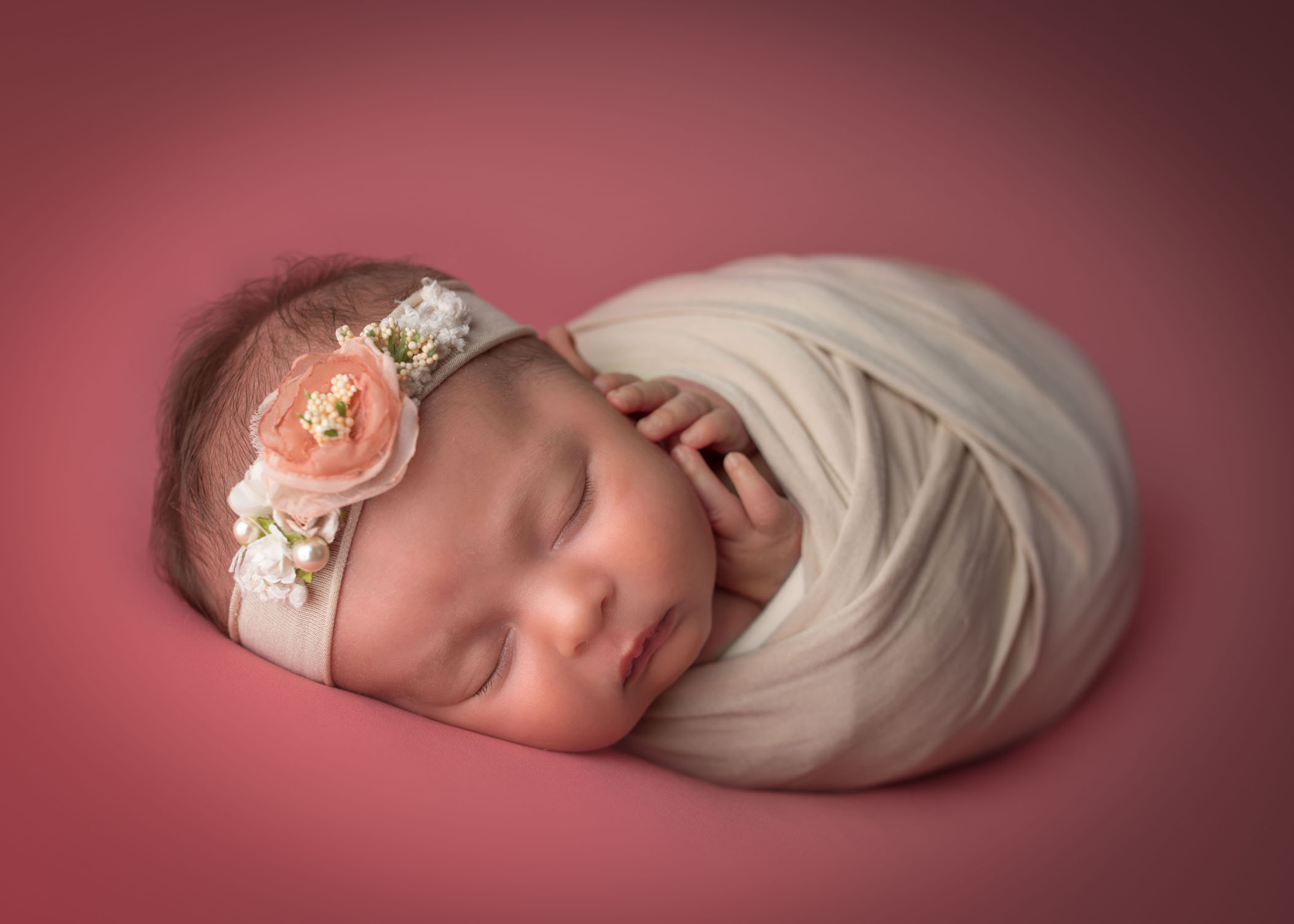 swaddled newborn baby girl asleep on bright coral background