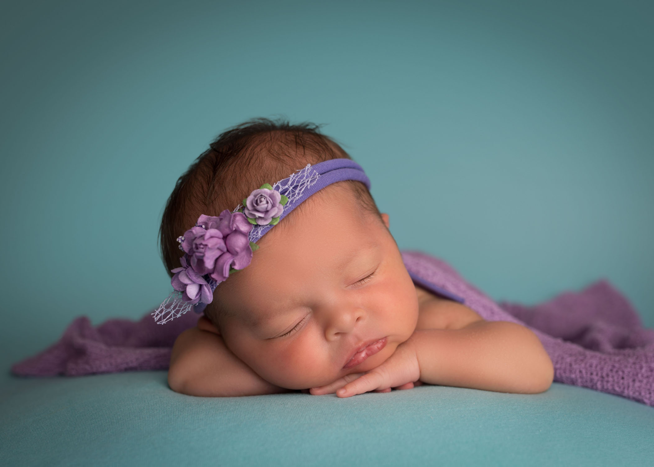 newborn baby girl sleeping with her head on her arms on teal blue with light purple headband