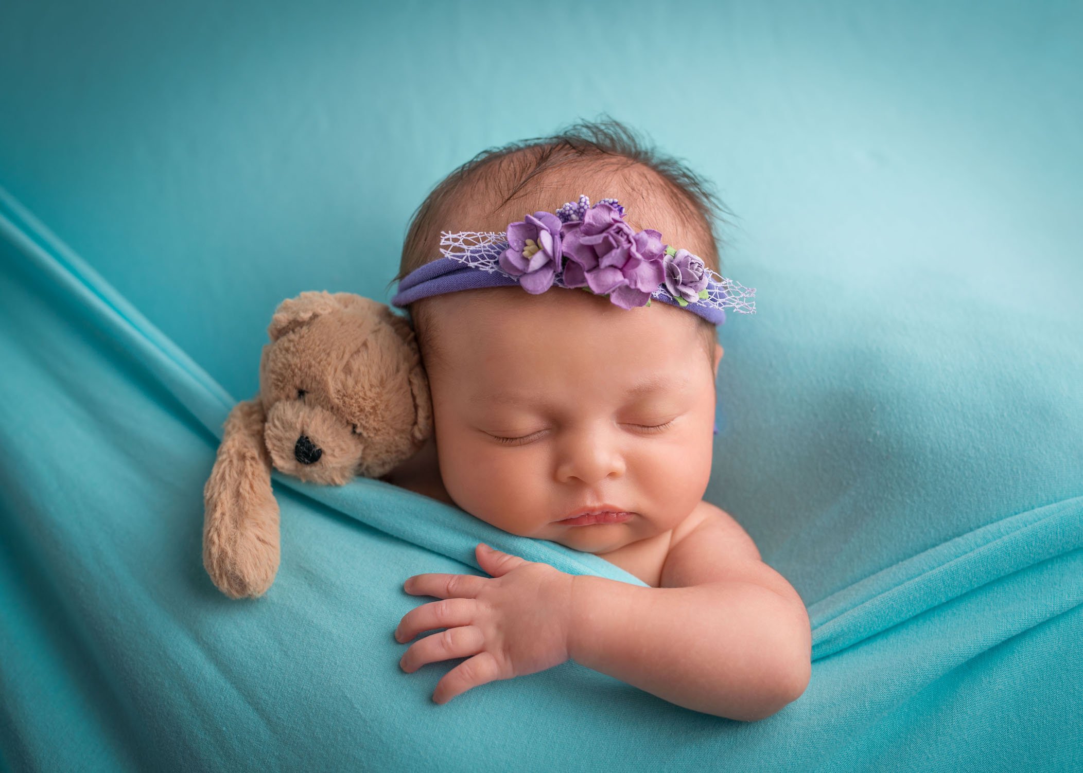 newborn baby girl sleeping on teal blue with her teddy bear