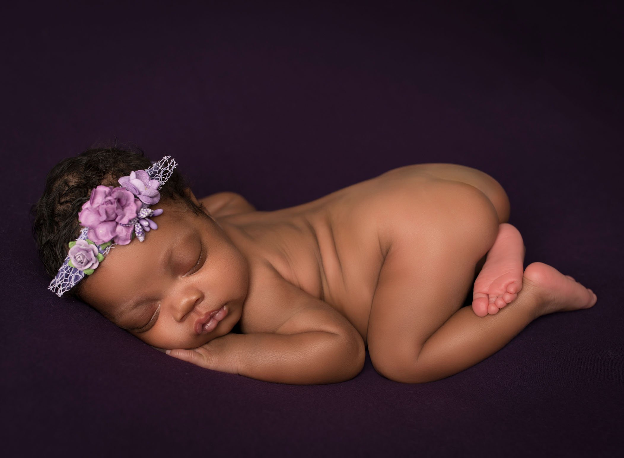 african-american newborn baby girl sleeping in bum up pose on purple background