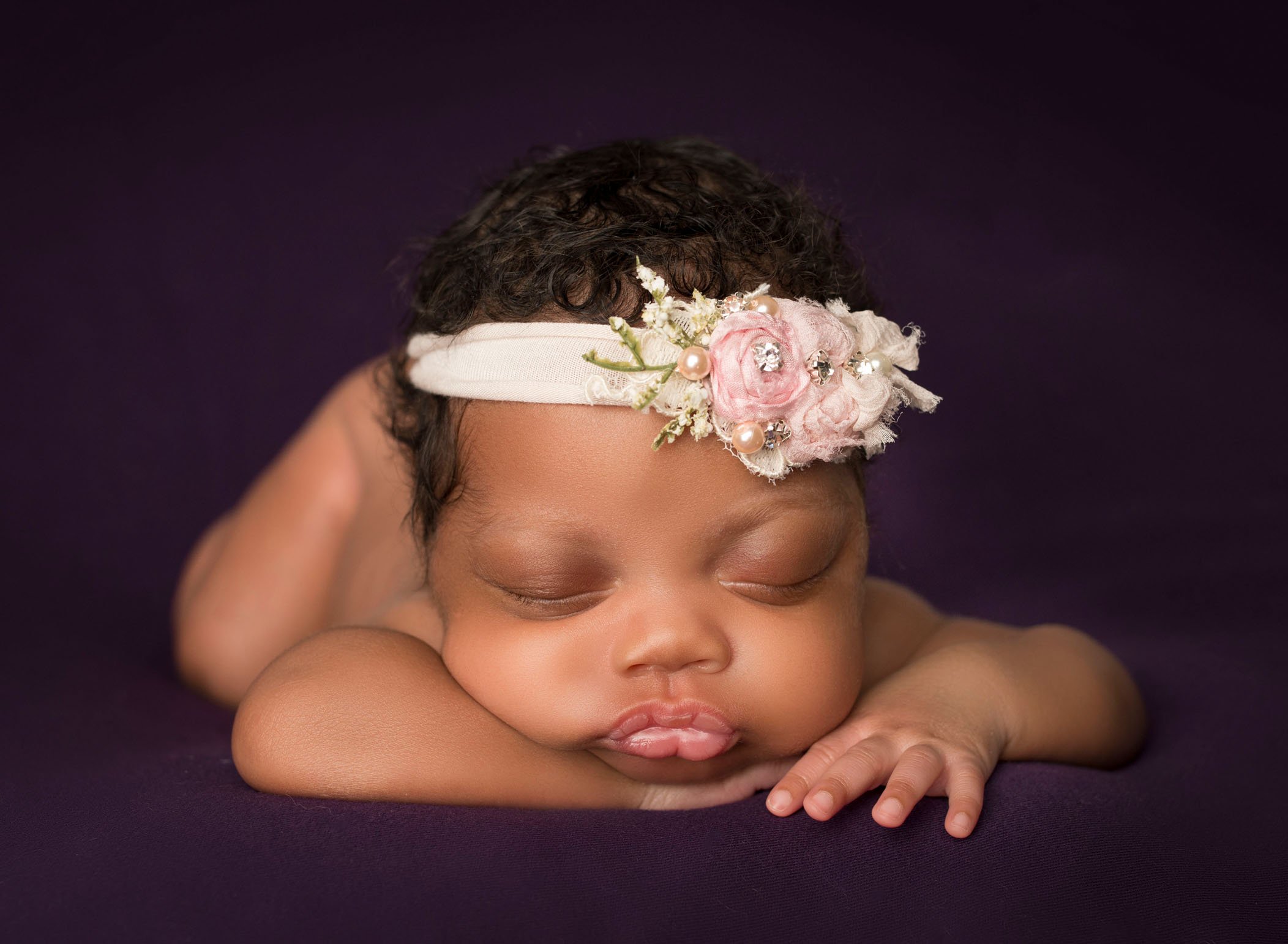 african-american newborn baby girl sleeping with her head on her hands on purple background
