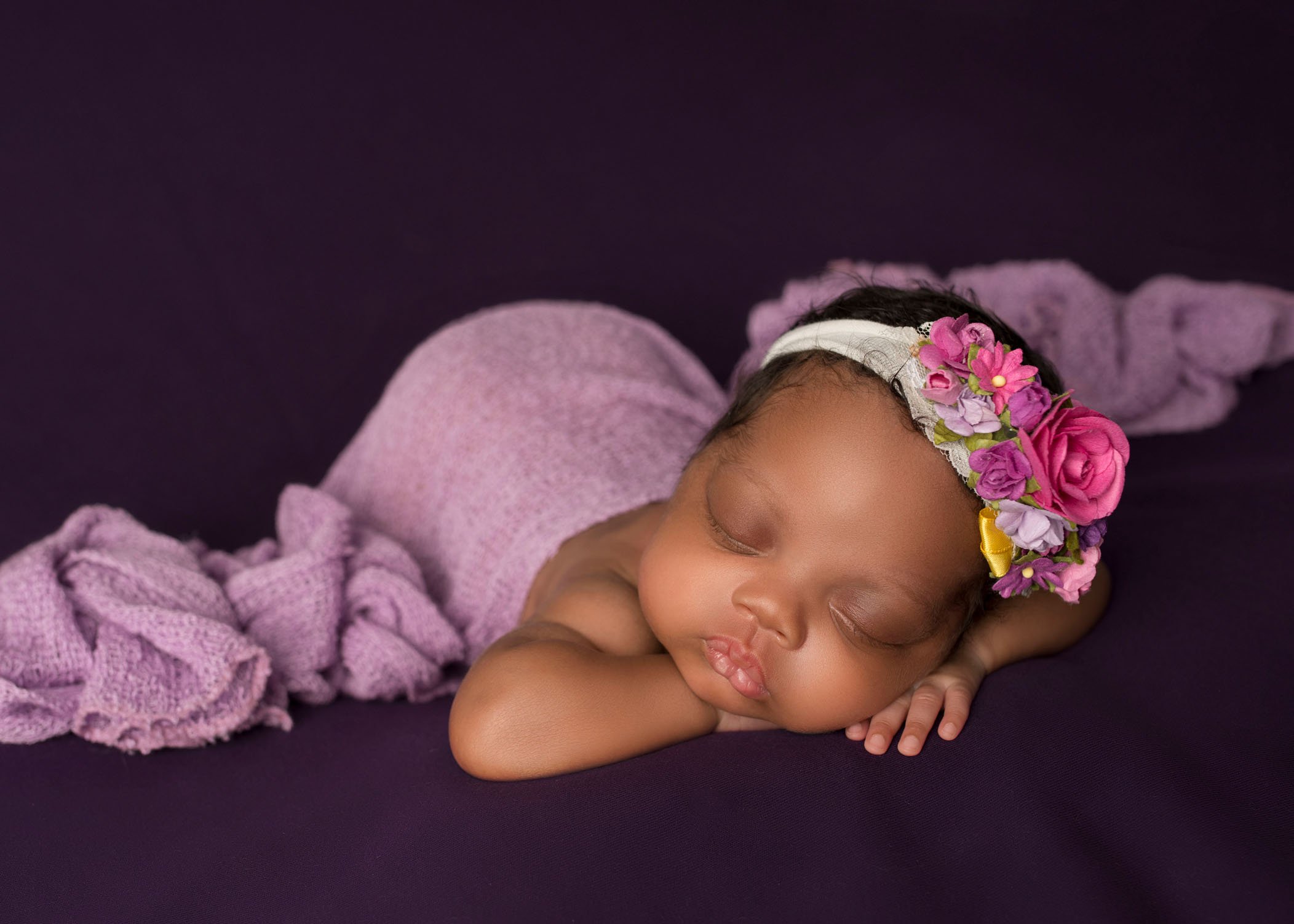 african-american newborn baby girl sleeping with her head on her hands draped in lavender blanket
