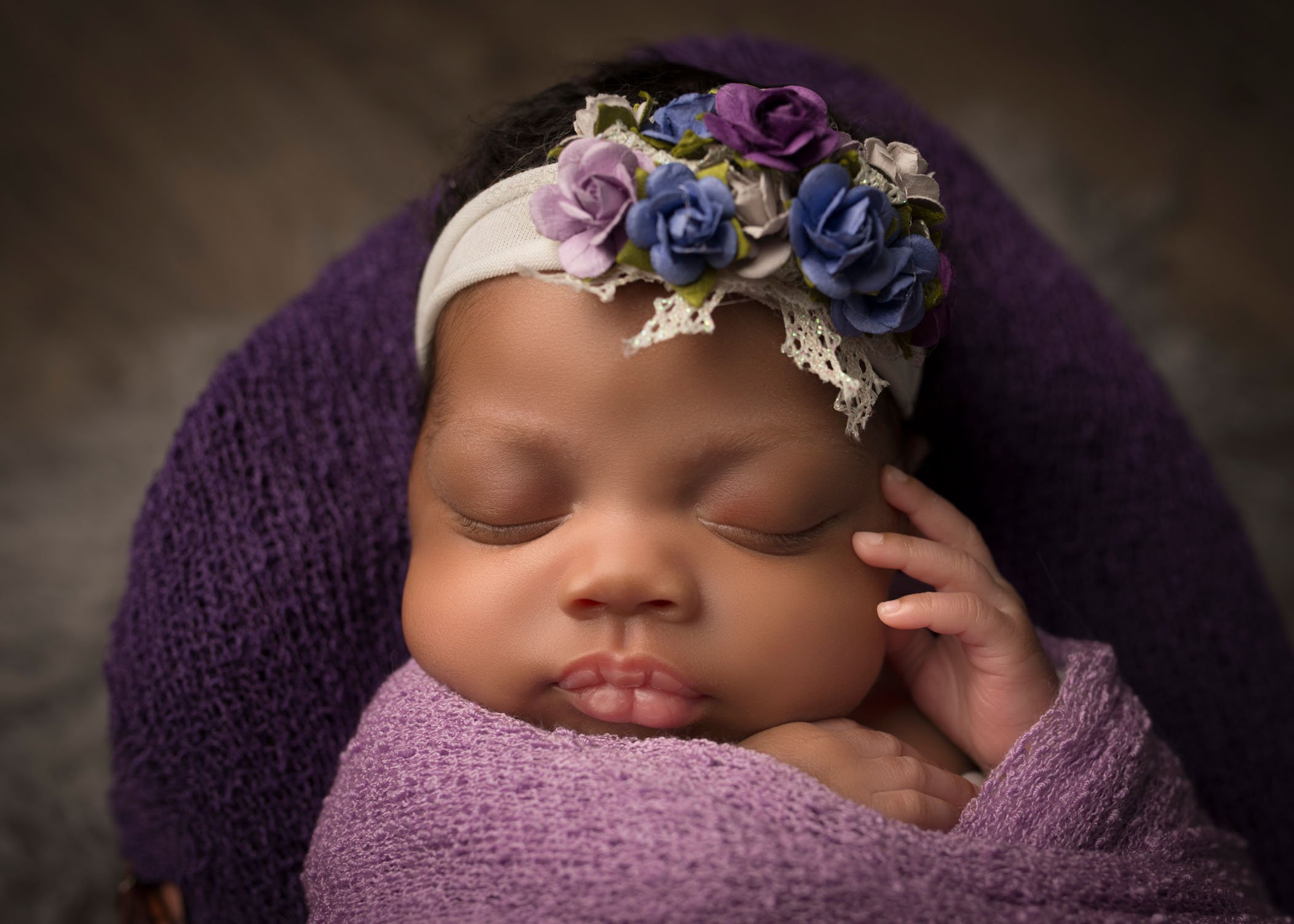 african-american newborn baby girl sleeping with hand by her cheek and floral headband on