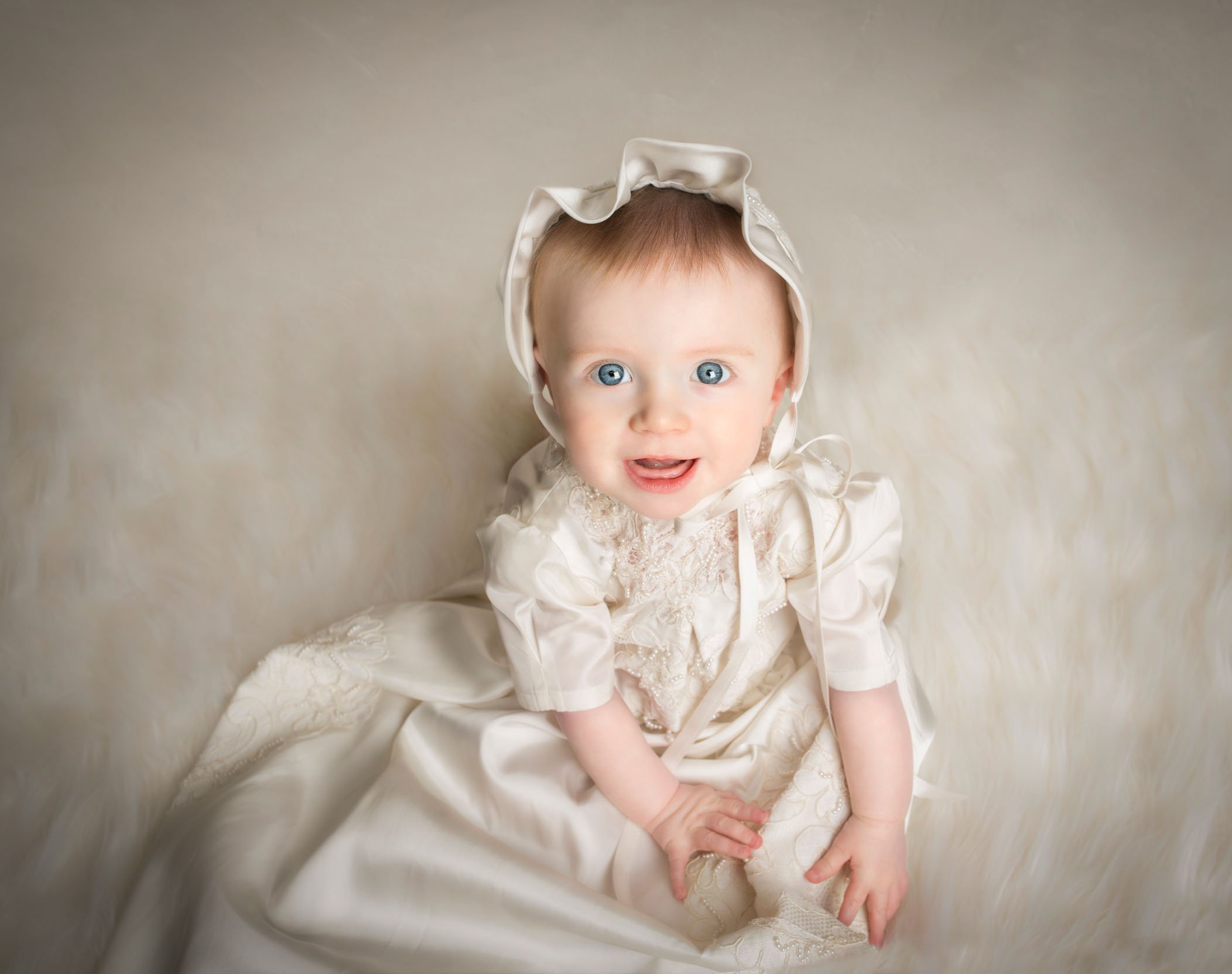6 mo old little girl dressed in her Christening gown looking at the camera