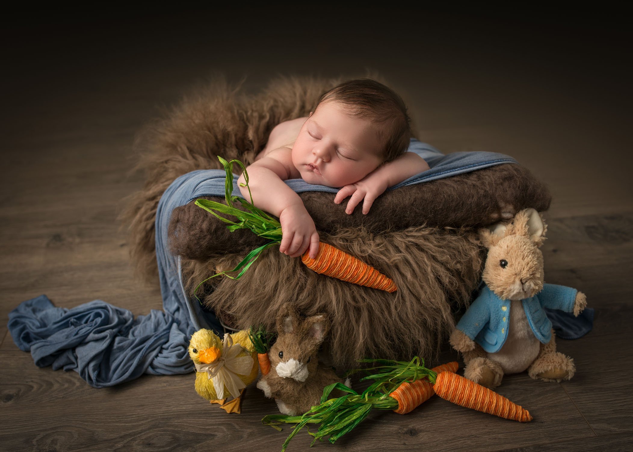newborn baby holding a carrot while sleeping with Peter Rabbit and his friends keeping watch
