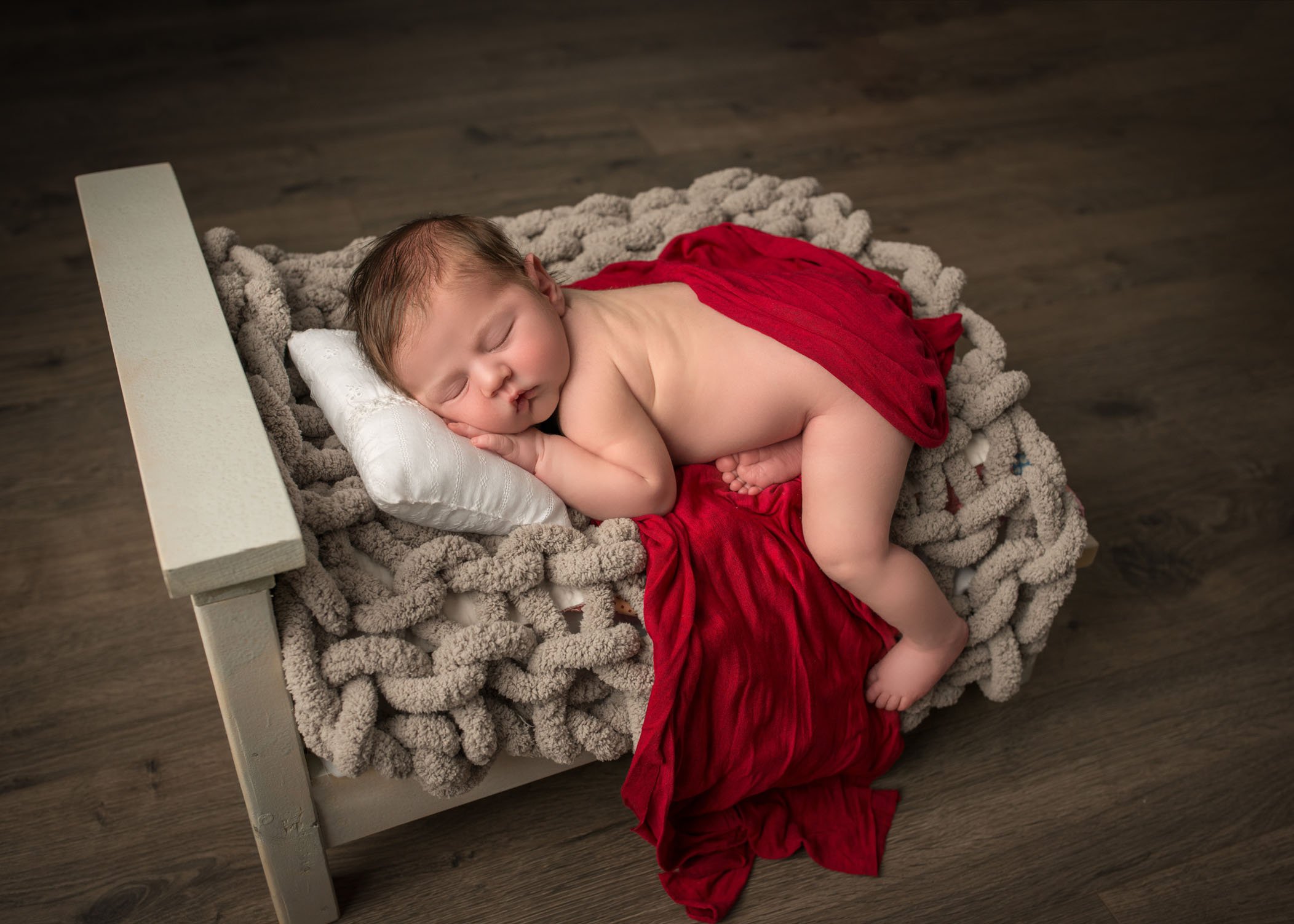newborn baby sleeping on his tummy on a doll sized bed