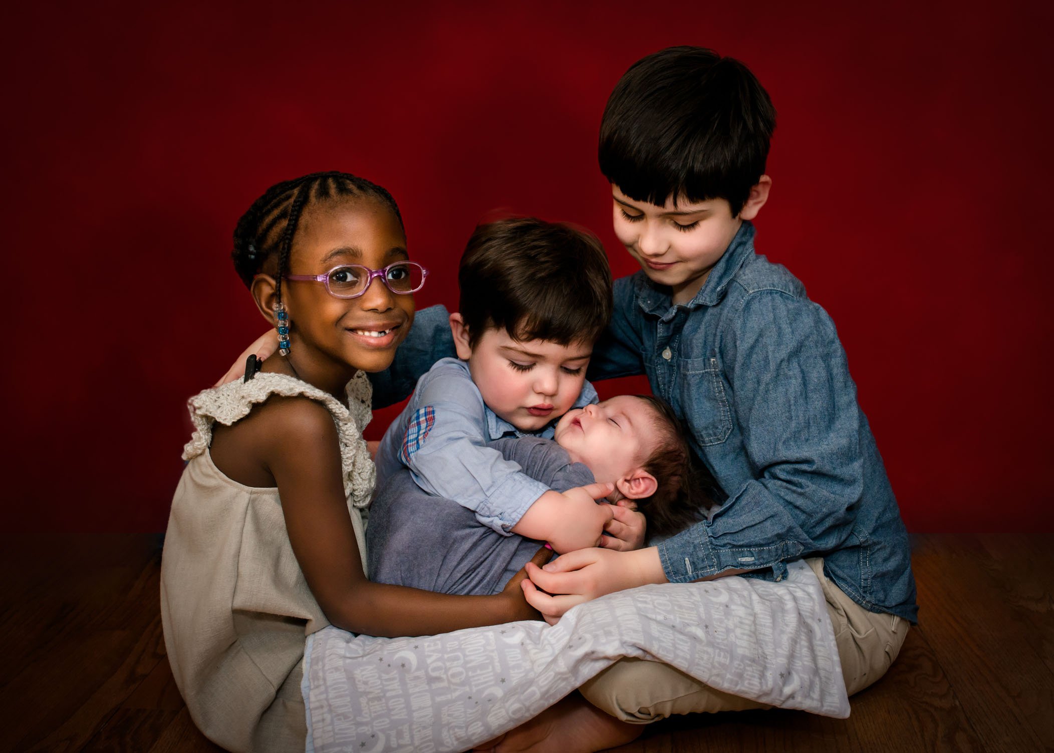 three siblings holding newborn baby in their laps