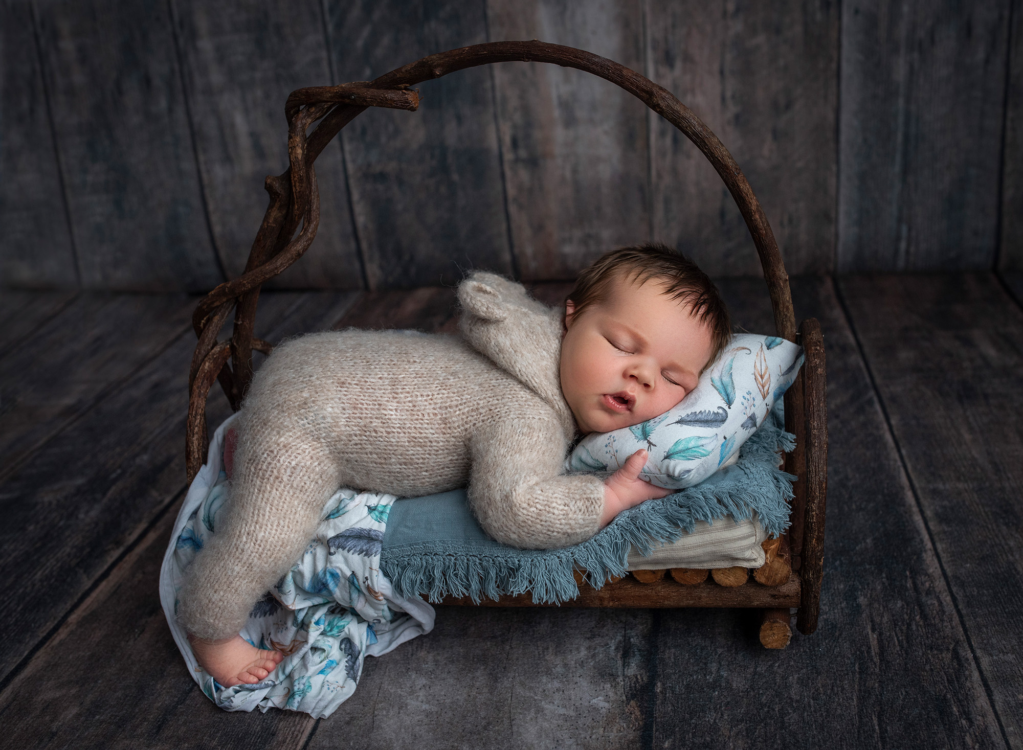 Nature Lover Newborn Photos newborn baby boy asleep in sweater romper with head on feather pillow laying on miniature wooden bed