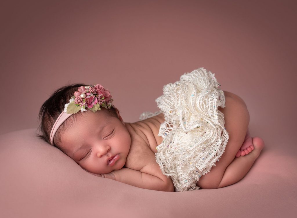 best time for newborn photos adorable newborn baby girl in bum up pose wearing a tutu and a pink floral headband on blush background best time to take newborn photos