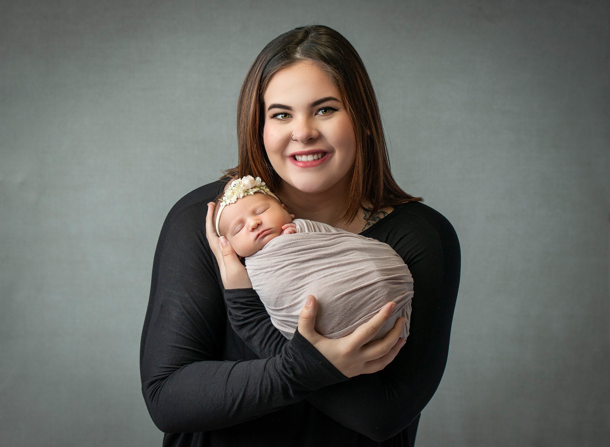 new mom cradling newborn baby girl swaddled in grey wrap