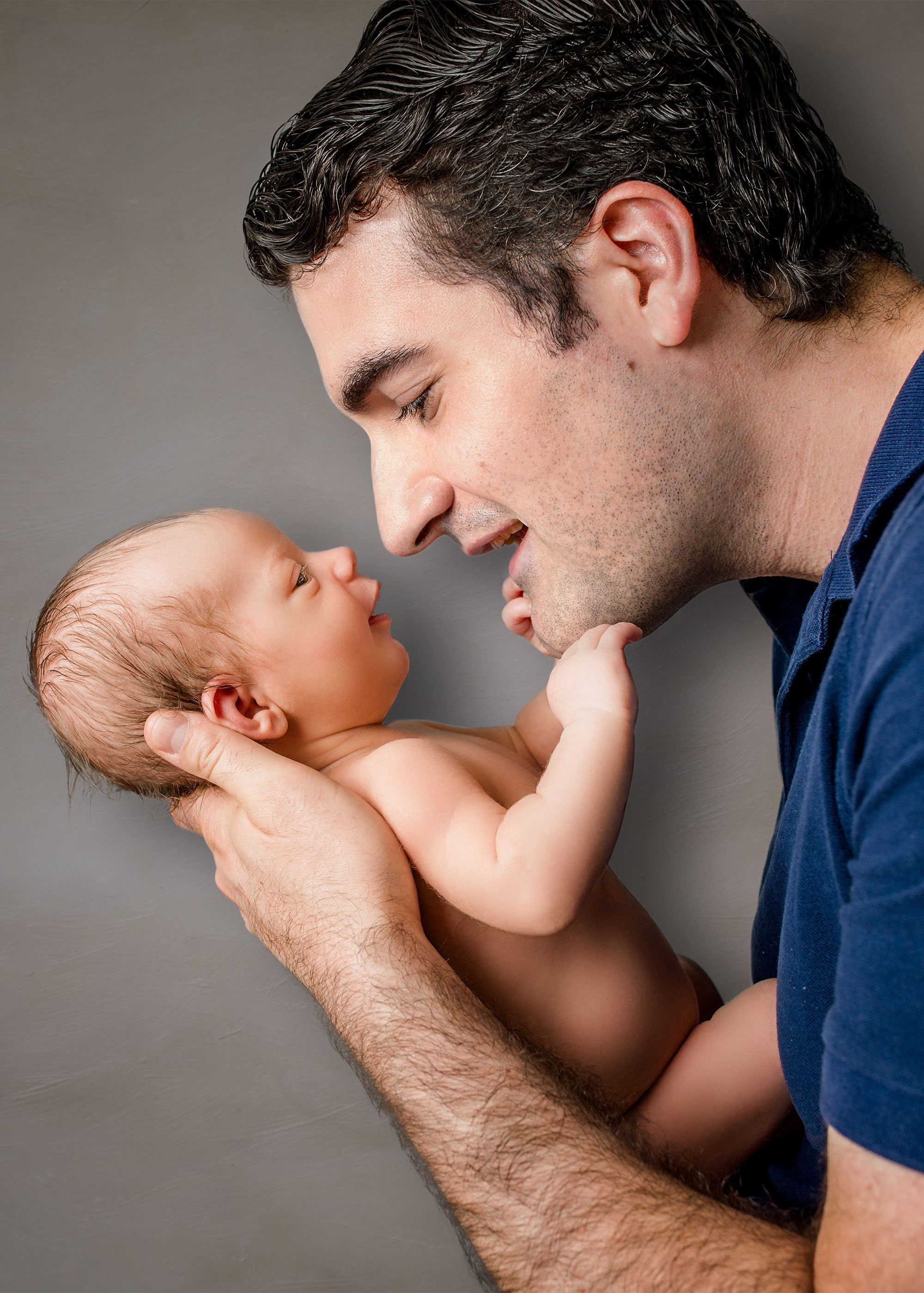 Daddy holding newborn boy face to face and smiling at each other
