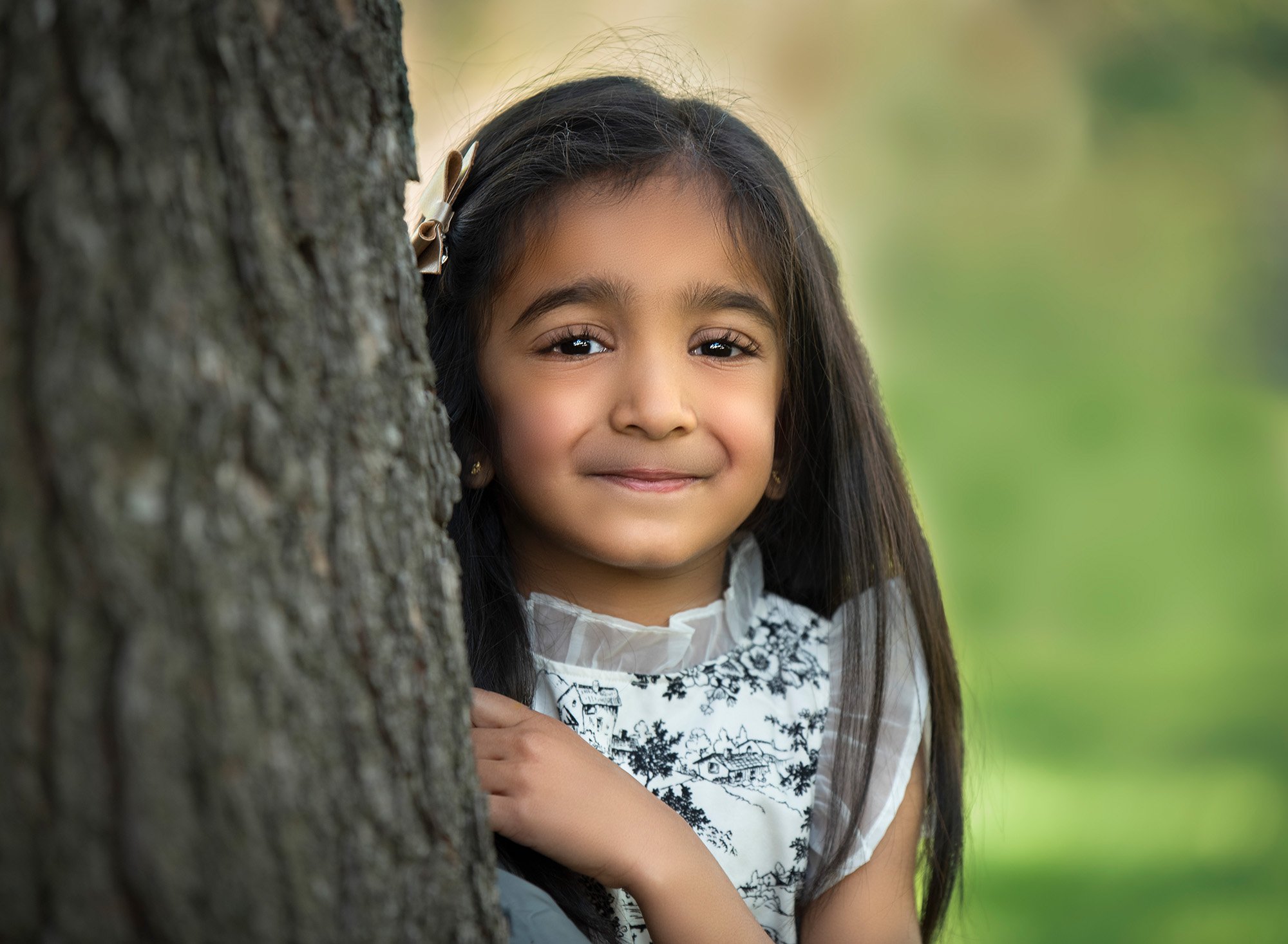 sweet little girl in black and white ruffled dress smiling while posing next to a tree