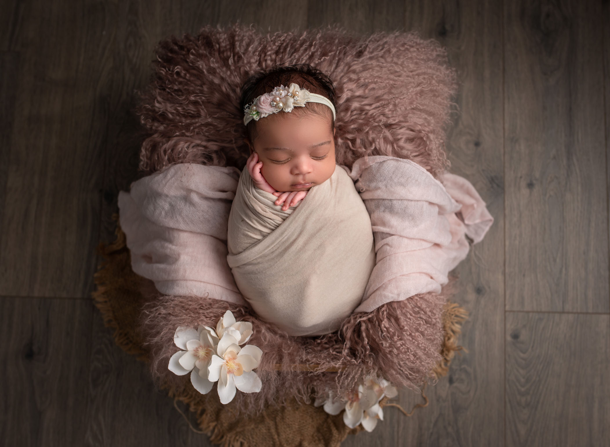 swaddled newborn girl asleep on pink fur with magnolia flowers