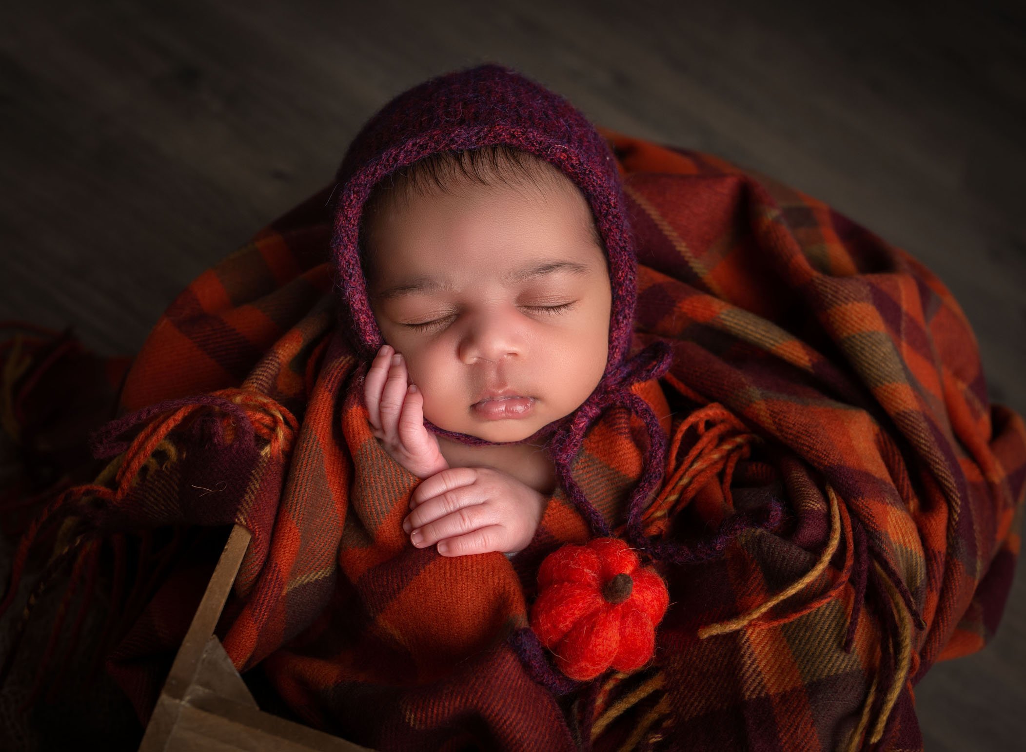 newborn wrapped in fall colors blanket sleeping with bonnet and baby pumpkin