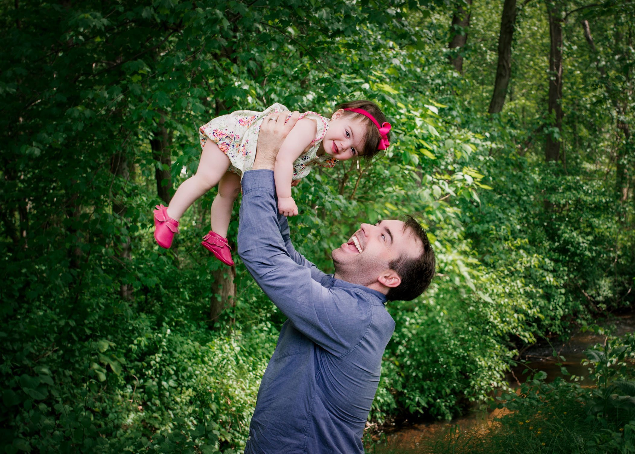Dad holding 1 year old baby girl up over his head and smiling