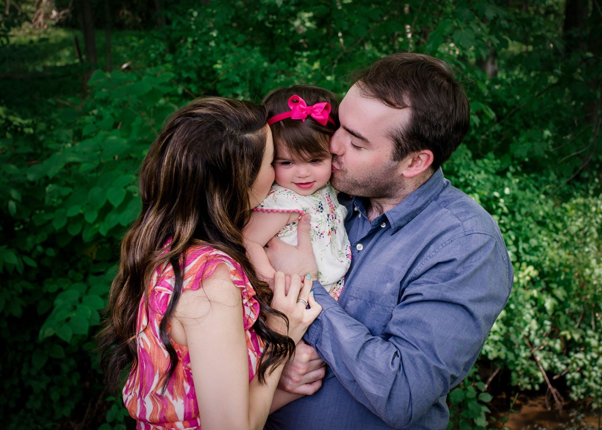 Mom and Dad kissing baby girl between them in the garden
