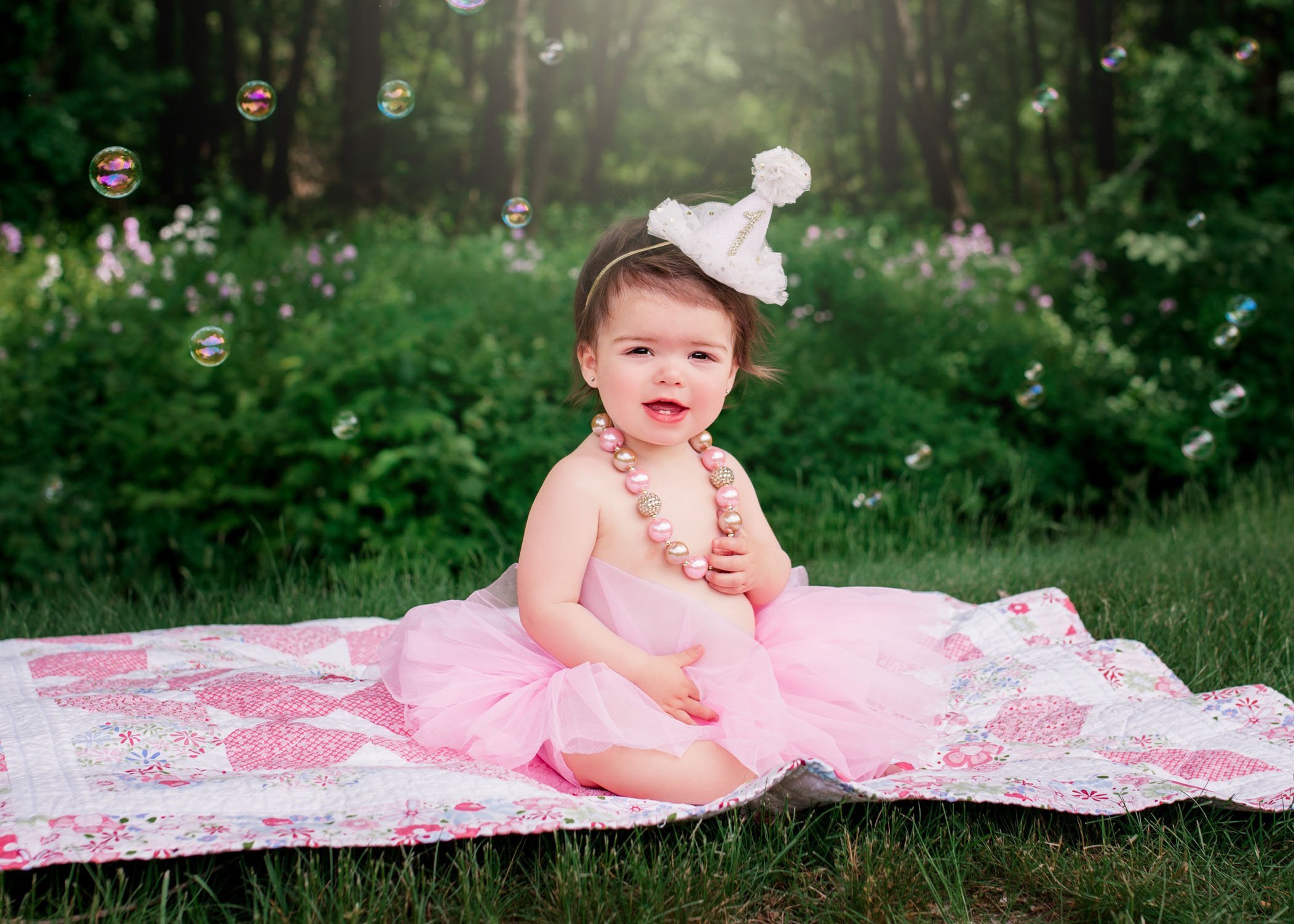 baby girl sitting up in the garden wearing a necklace and tutu surrounded by bubbles