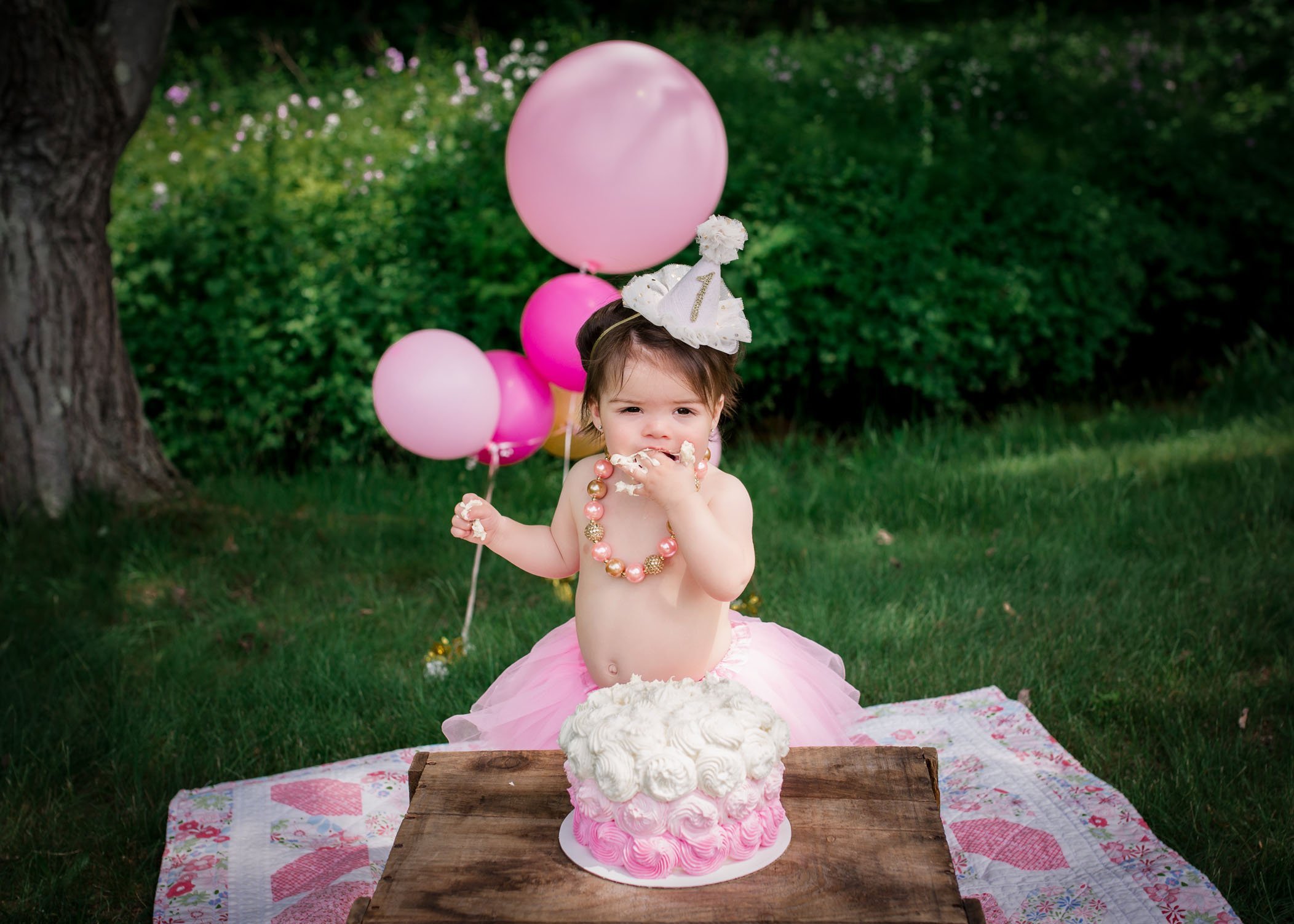 little girl wearing a necklace and tutu eating cake with her hands
