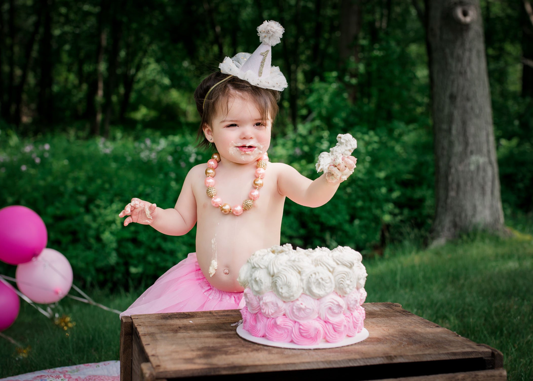 one year old girl holding out a piece of cake from her cake smash session